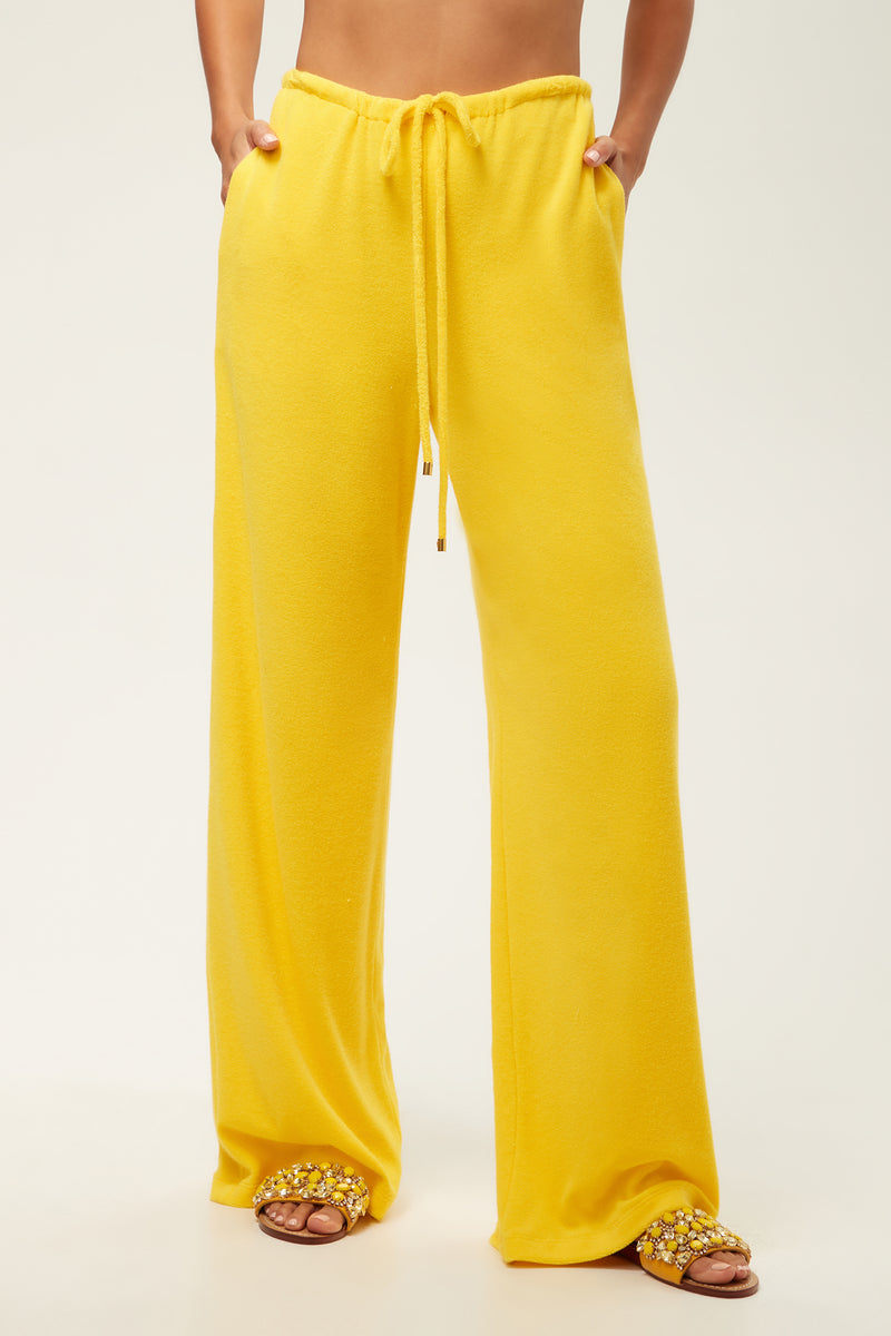A person wearing the Linsk Wide-Leg Pant - Poolside Terry in Desert Sun and embellished slide sandals stands against a plain light background; only the lower half is visible.