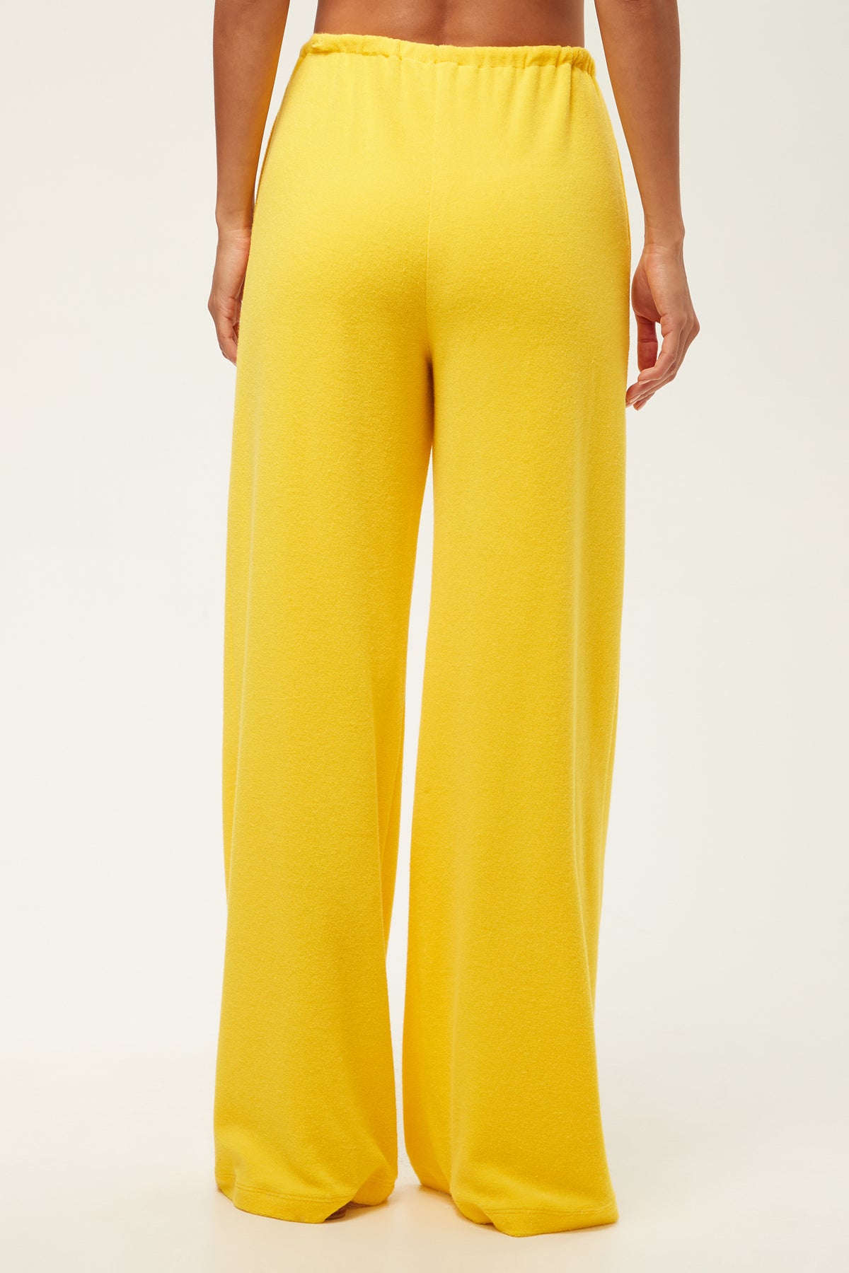 A person faces away, wearing the Linsk Wide-Leg Pant - Poolside Terry featuring a bright yellow hue, high waist, wide legs, and an elastic waistband. The background is plain white.