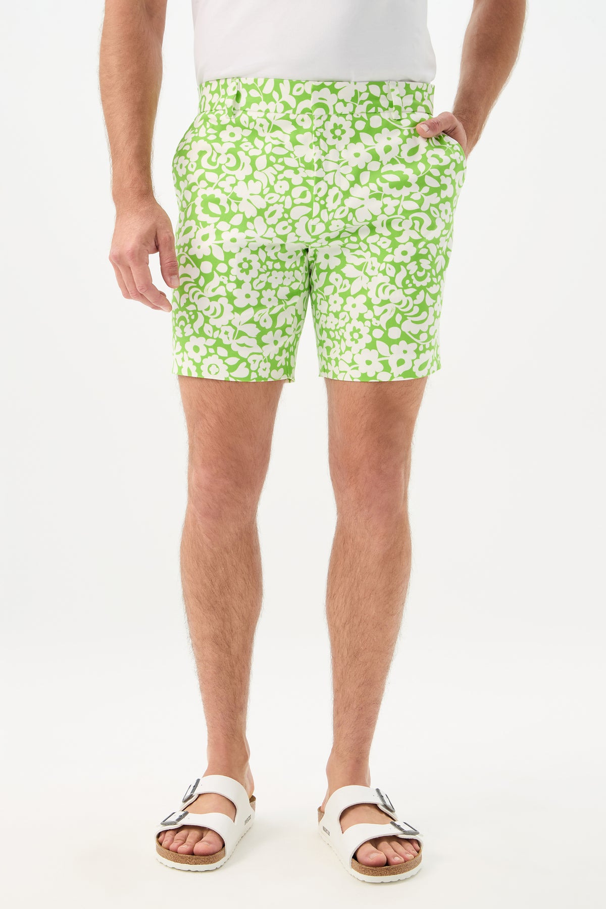 Wearing the Lawrence Short - Poolside Gossip in Serene Green, a person stands against a plain white background. They also wear a white shirt and sandals; the photo is cropped from the shoulders down.
