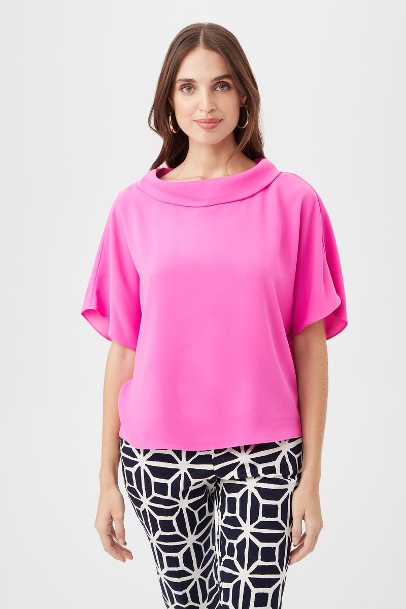 A woman wears the Honeysuckle Boatneck Dolman-Sleeve Top in Snapdragon, paired with black-and-white geometric patterned pants, standing facing forward against a plain white background.