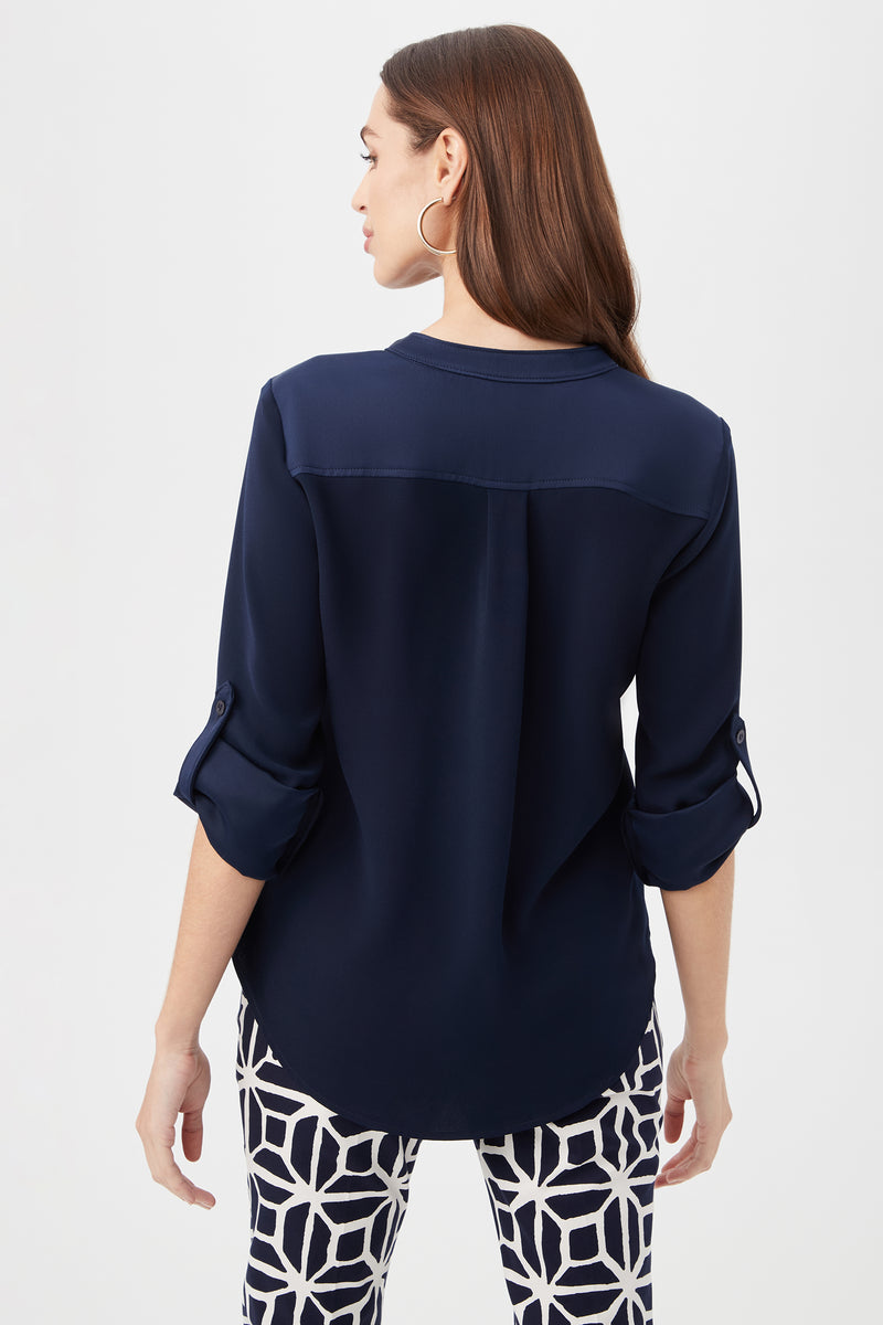A woman with long brown hair, seen from the back against a white background, wears the Kaiko 3/4-Sleeve Half-Zip Top in navy blue and black-and-white geometric patterned pants.