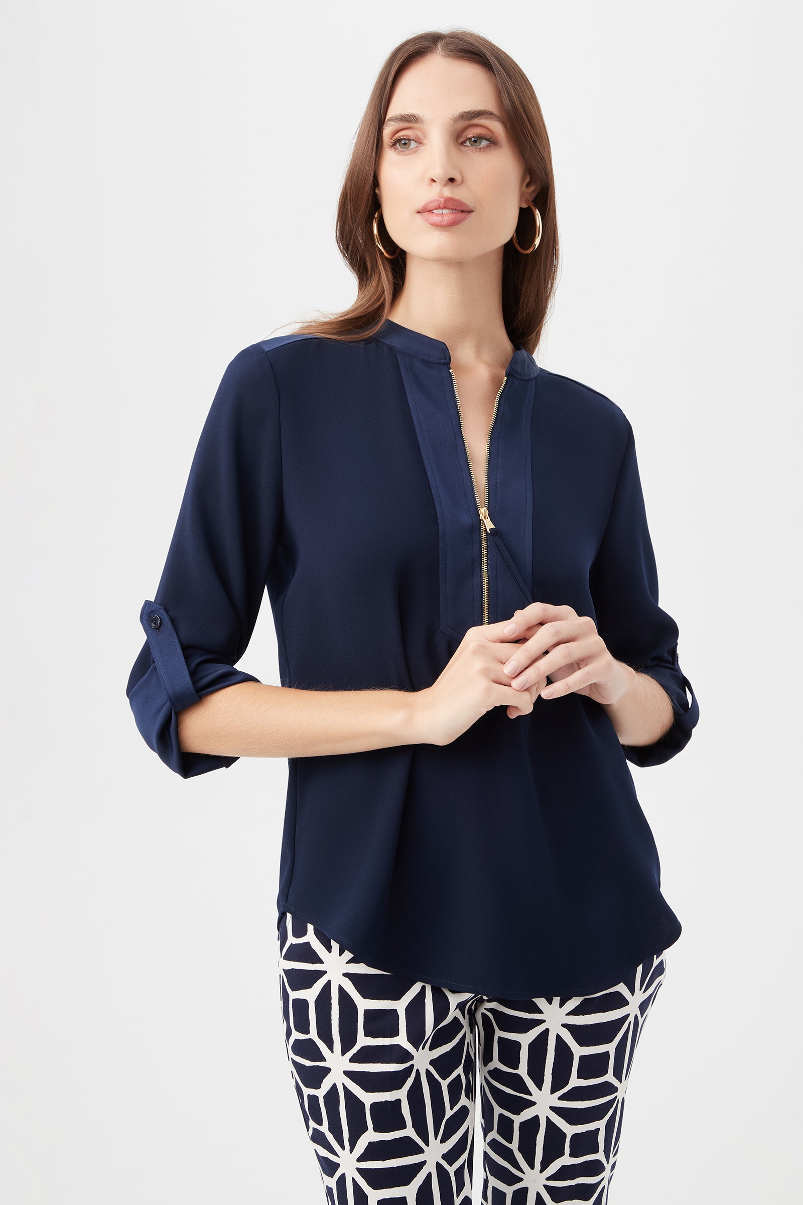 A woman with long brown hair stands against a plain white background wearing the Kaiko 3/4-Sleeve Half-Zip Top in indigo and patterned black-and-white pants, looking slightly to the side.