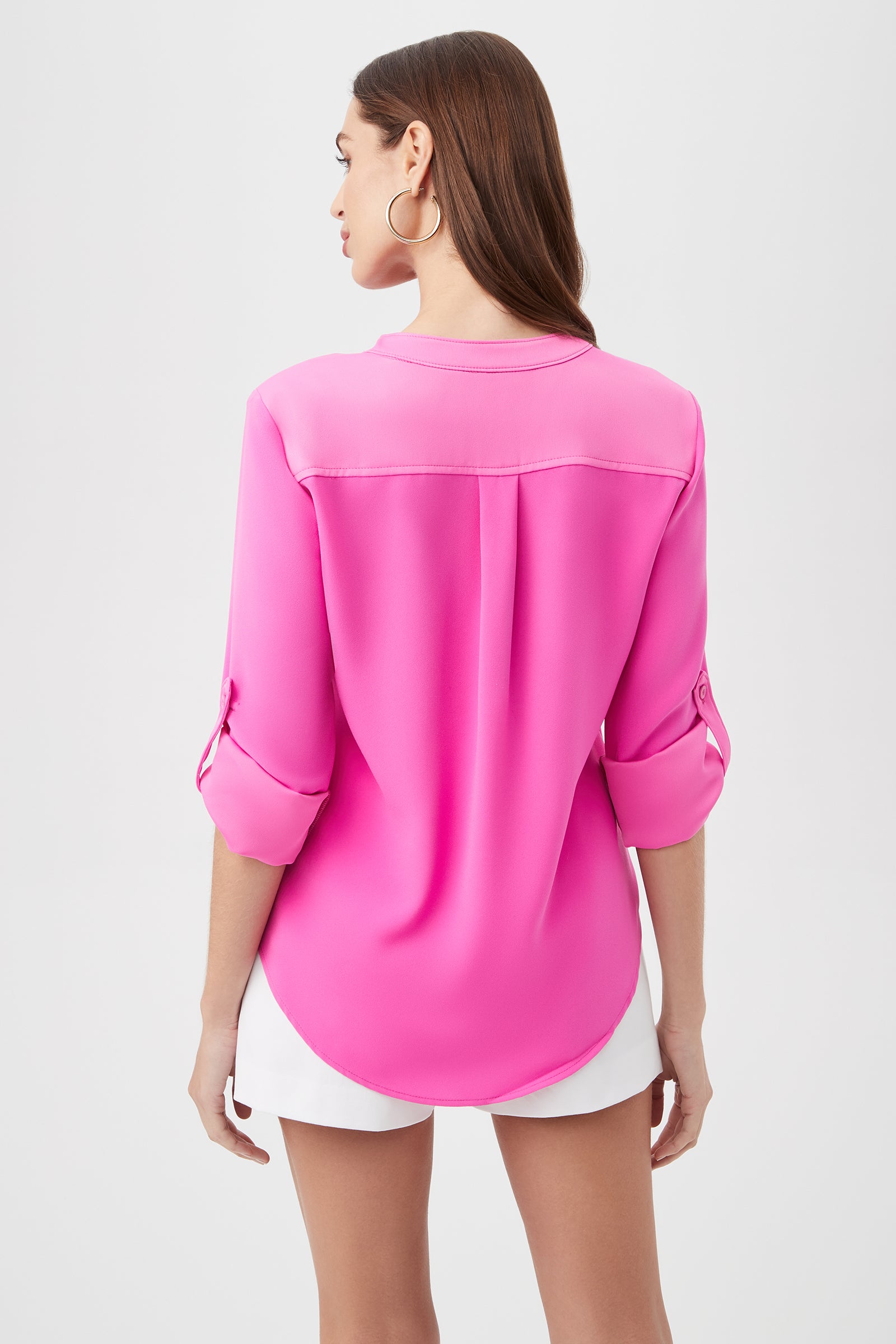 A woman with straight brown hair wears the Kaiko 3/4-Sleeve Half-Zip Top in bright pink and white shorts, shown from the back against a plain white background.
