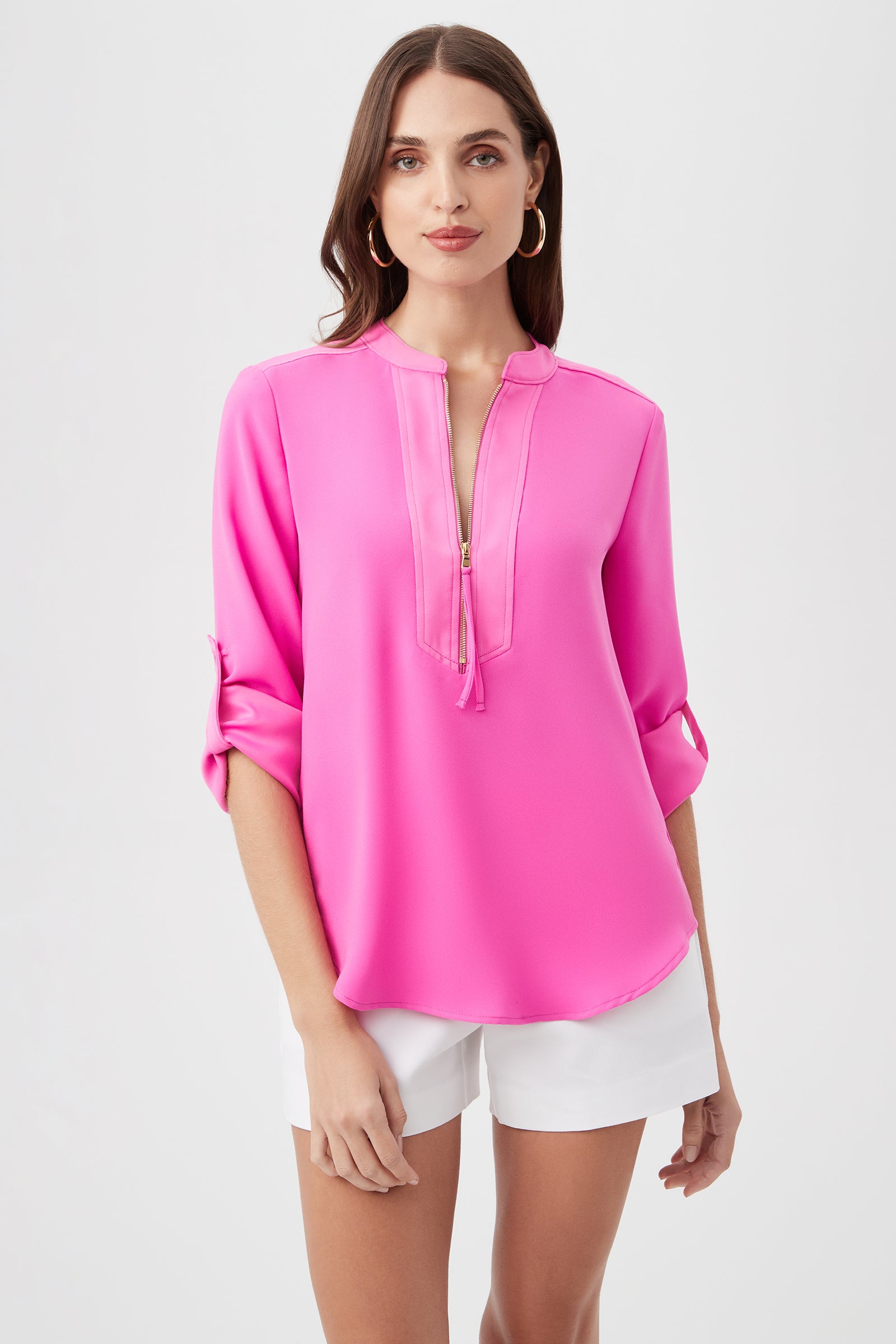 A woman with long brown hair wears the Kaiko 3/4-Sleeve Half-Zip Top in Snapdragon and white shorts, standing against a plain light background and looking at the camera with a neutral expression.