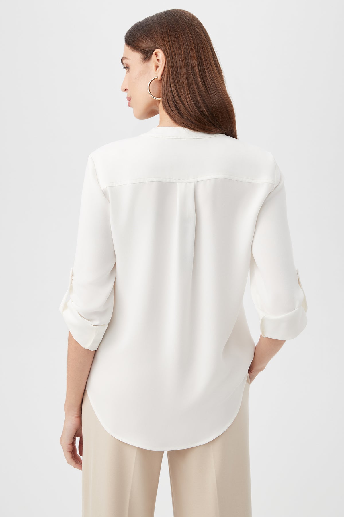 A woman with long brown hair, wearing the Kaiko 3/4-Sleeve Half-Zip Top and beige pants, faces away from the camera against a plain light background.