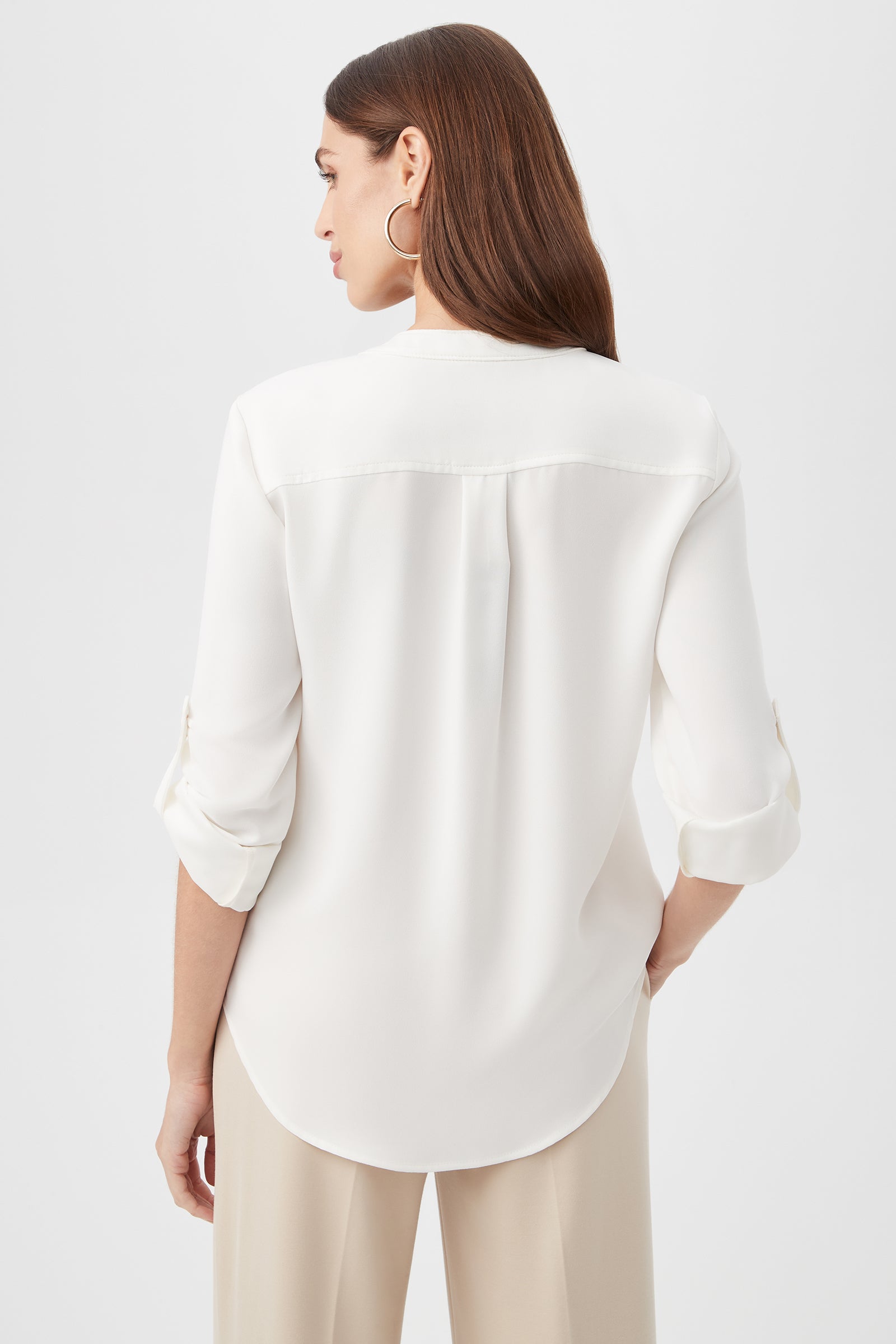 A woman with long brown hair, wearing the Kaiko 3/4-Sleeve Half-Zip Top and beige pants, faces away from the camera against a plain light background.