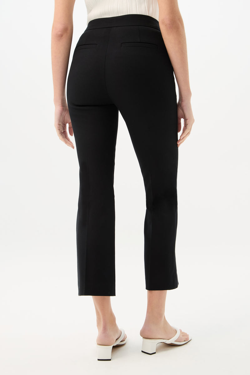A person is seen from the back against a plain white background, wearing black Lulu Cropped Pant - Cotton Bi-Stretch, white heeled sandals, and a sleeveless white top.