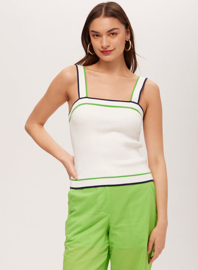 A woman poses confidently in the Break Point Contrast Trim Knit Cami Top—a white sleeveless knit cami with navy and green trim—paired with bright green high-waisted pants, hoop earrings, and long brown hair.
