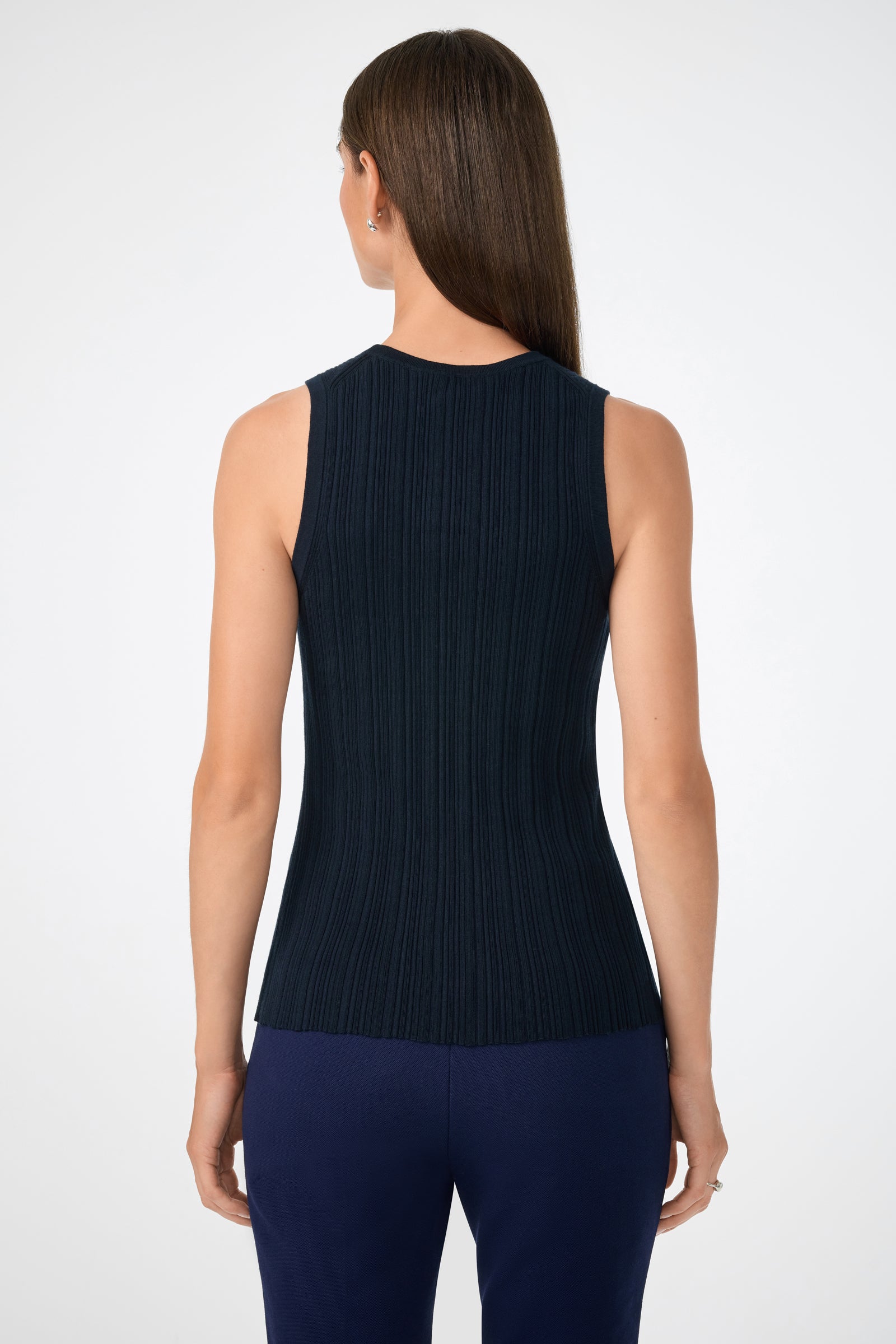 A woman with straight brown hair, seen from the back, wears the sleeveless Gibraltar Tank in dark navy and matching navy pants against a plain white background.