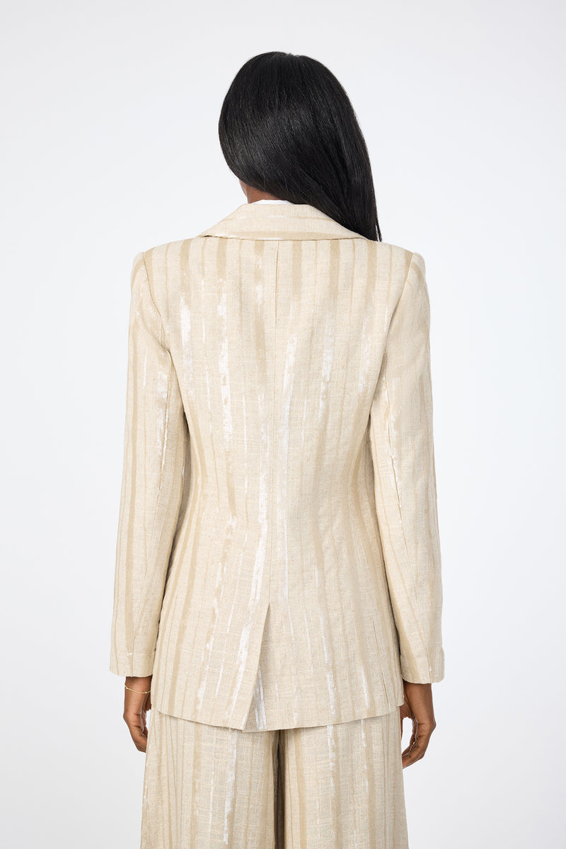 A person with long dark hair faces away, wearing the Alternates 2 Blazer‚Äö√Ñ√Æa light beige, shimmery pinstripe suit jacket with matching pants‚Äö√Ñ√Æset against a plain white background.