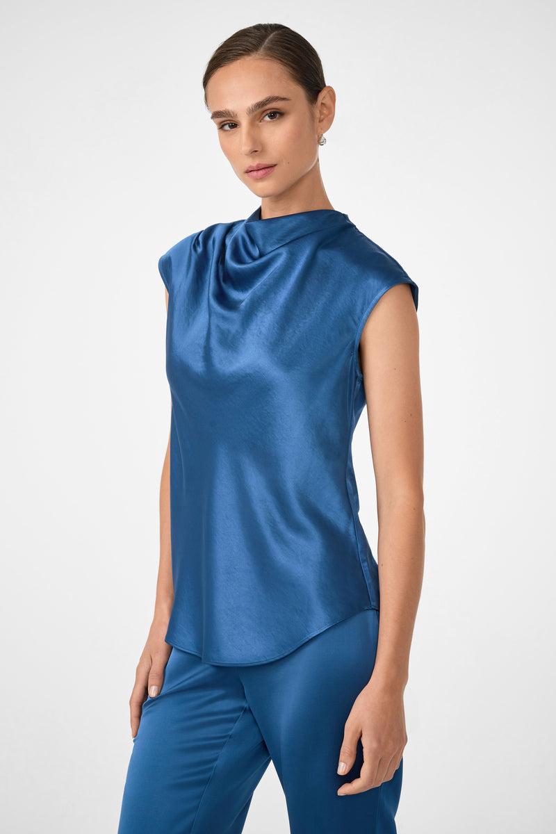A woman wearing the Mikan Sleeveless Top in shiny blue satin stands against a plain white background, looking at the camera with a neutral expression.