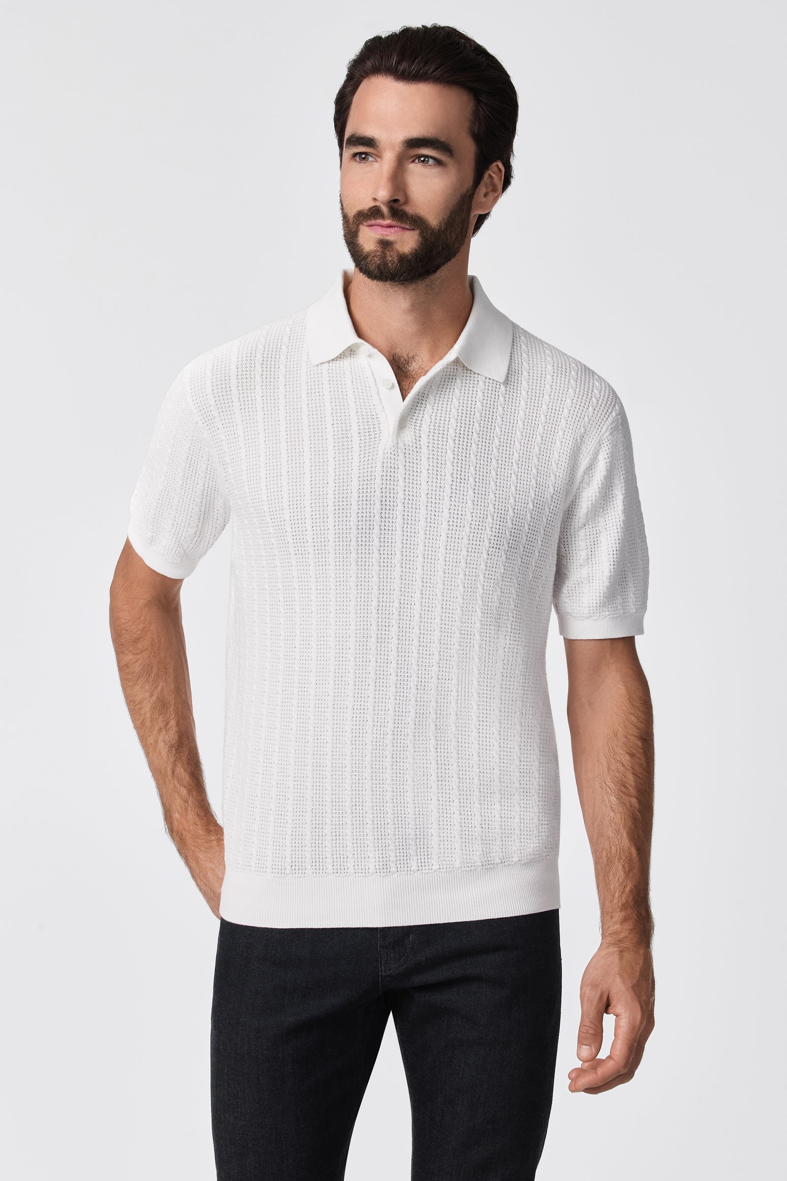 A man with dark hair and a beard wears the Asher Short-Sleeve Polo in textured white and black pants, standing against a plain white background.