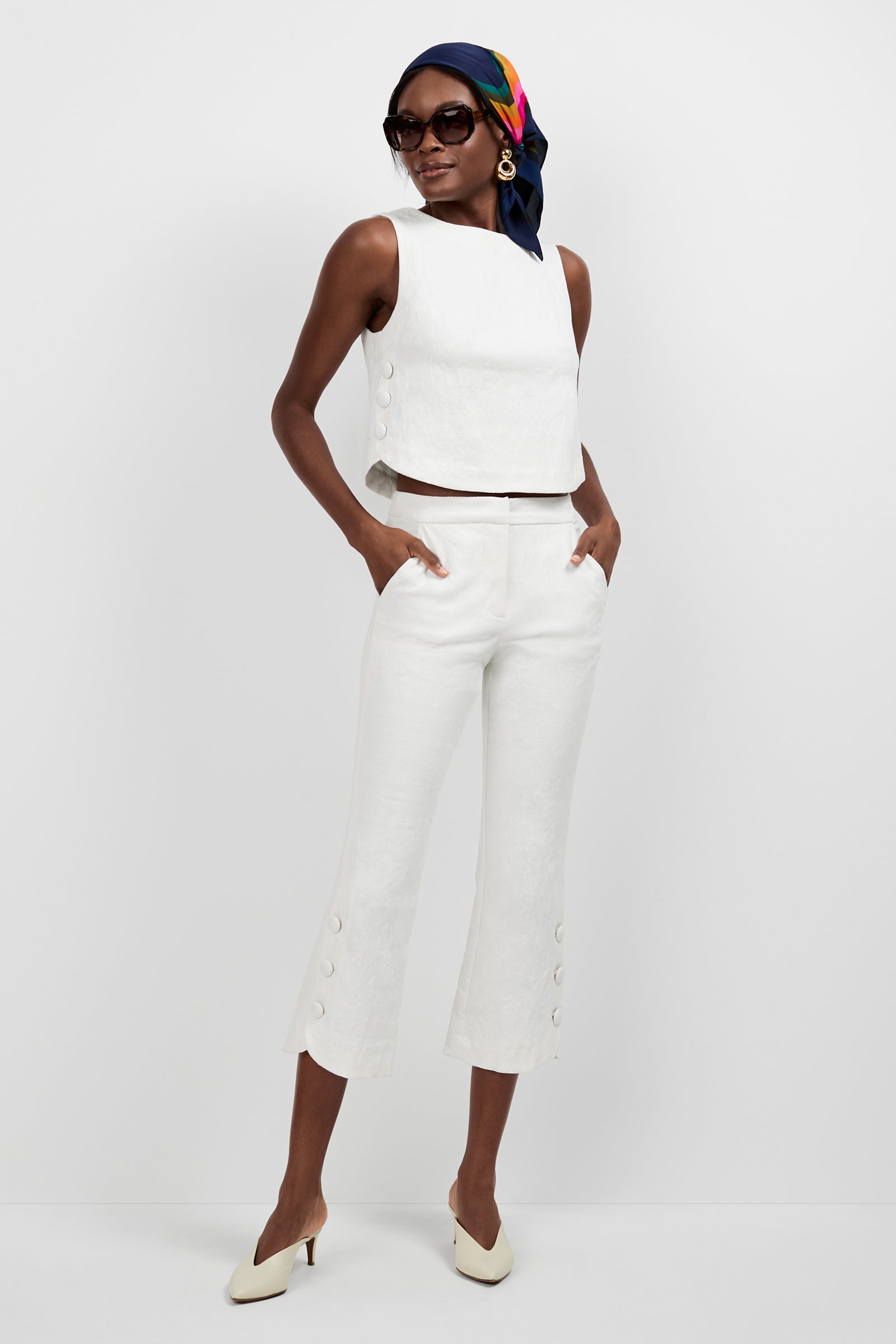 A woman poses against a white background wearing the Siara Button Side Top, matching cropped pants, white heels, sunglasses, gold hoop earrings, and a colorful scarf tied around her head.
