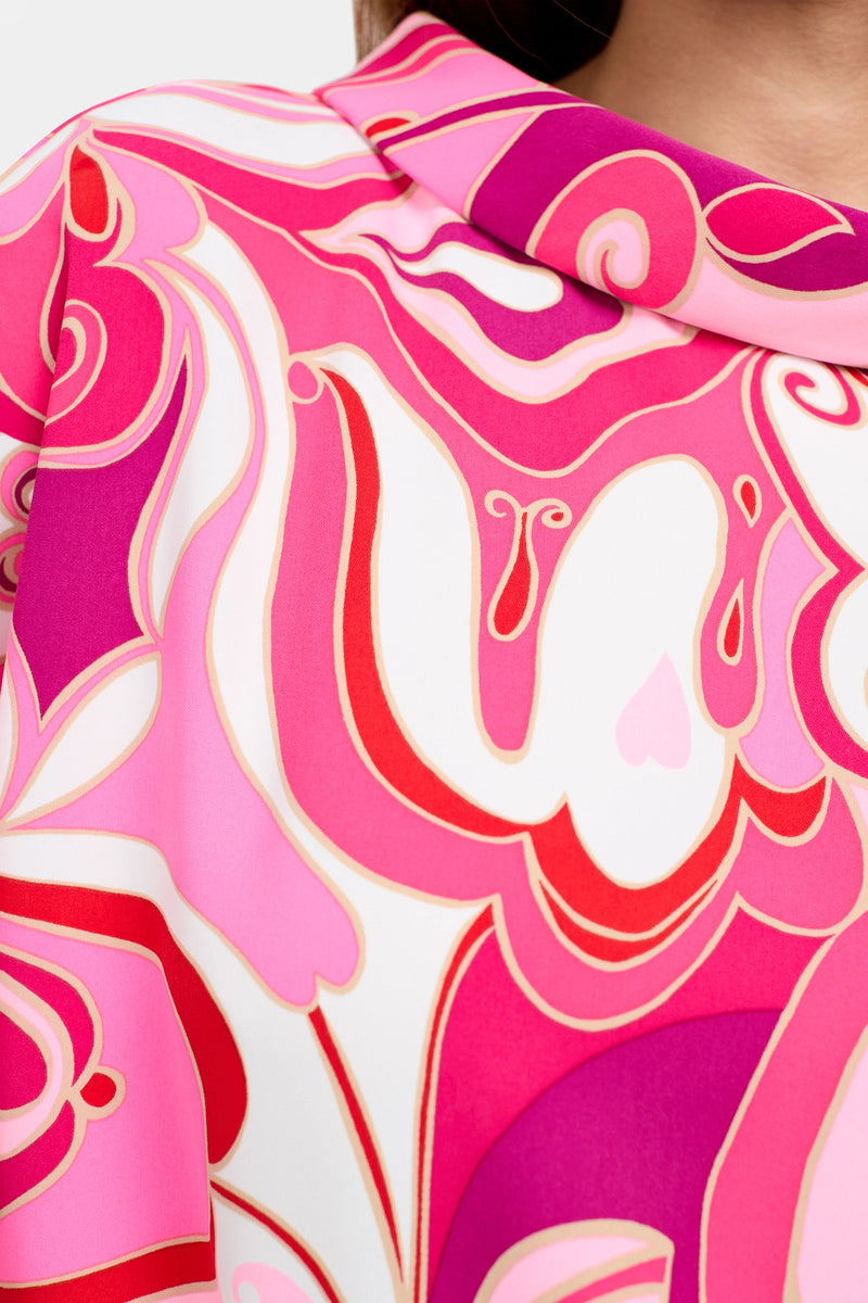 Close-up of the Honeysuckle Boatneck Top's fabric, showcasing a vibrant abstract pattern in pink, red, and white with swirling shapes—some edged in gold. The fabric is featured as part of this stylish garment.