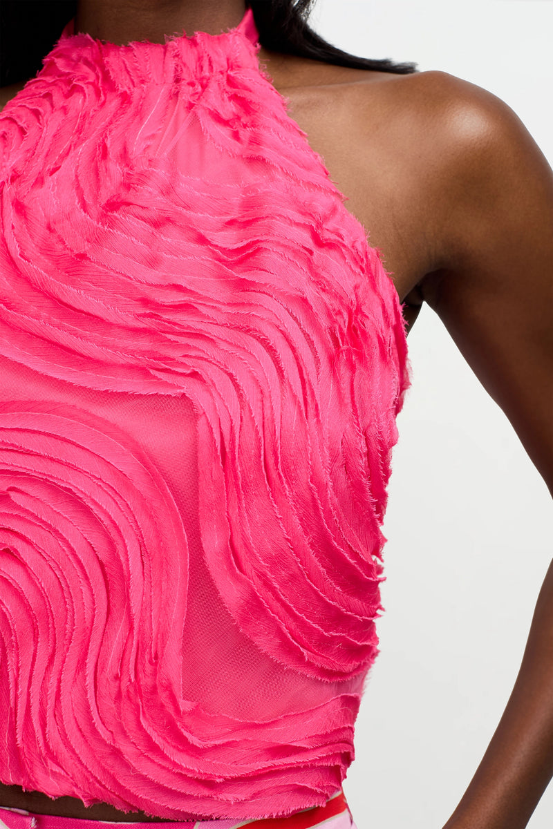 A close-up of the Myka Organza Halter Top, a sleeveless bright pink top with textured swirling patterns, semi-sheer fabric, and a high neckline, worn by a person with dark skin.