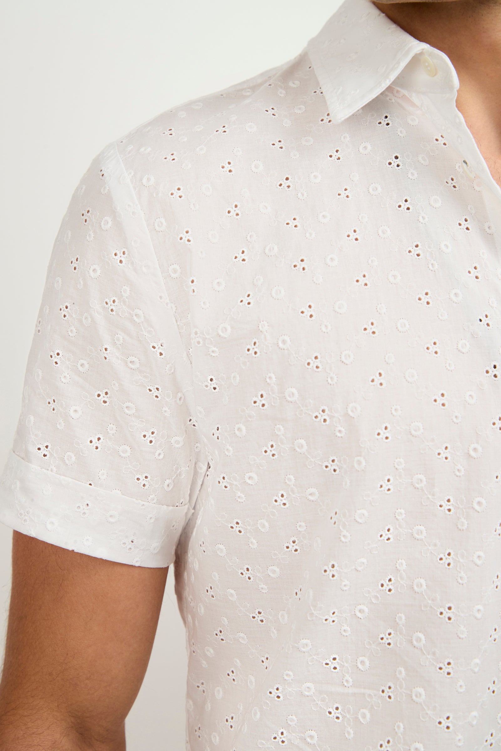 A person wears the Branson Short-Sleeve Shirt—a white, collared top with eyelet embroidery and small circular patterns. The image captures the upper torso and part of the arm against a plain background.
