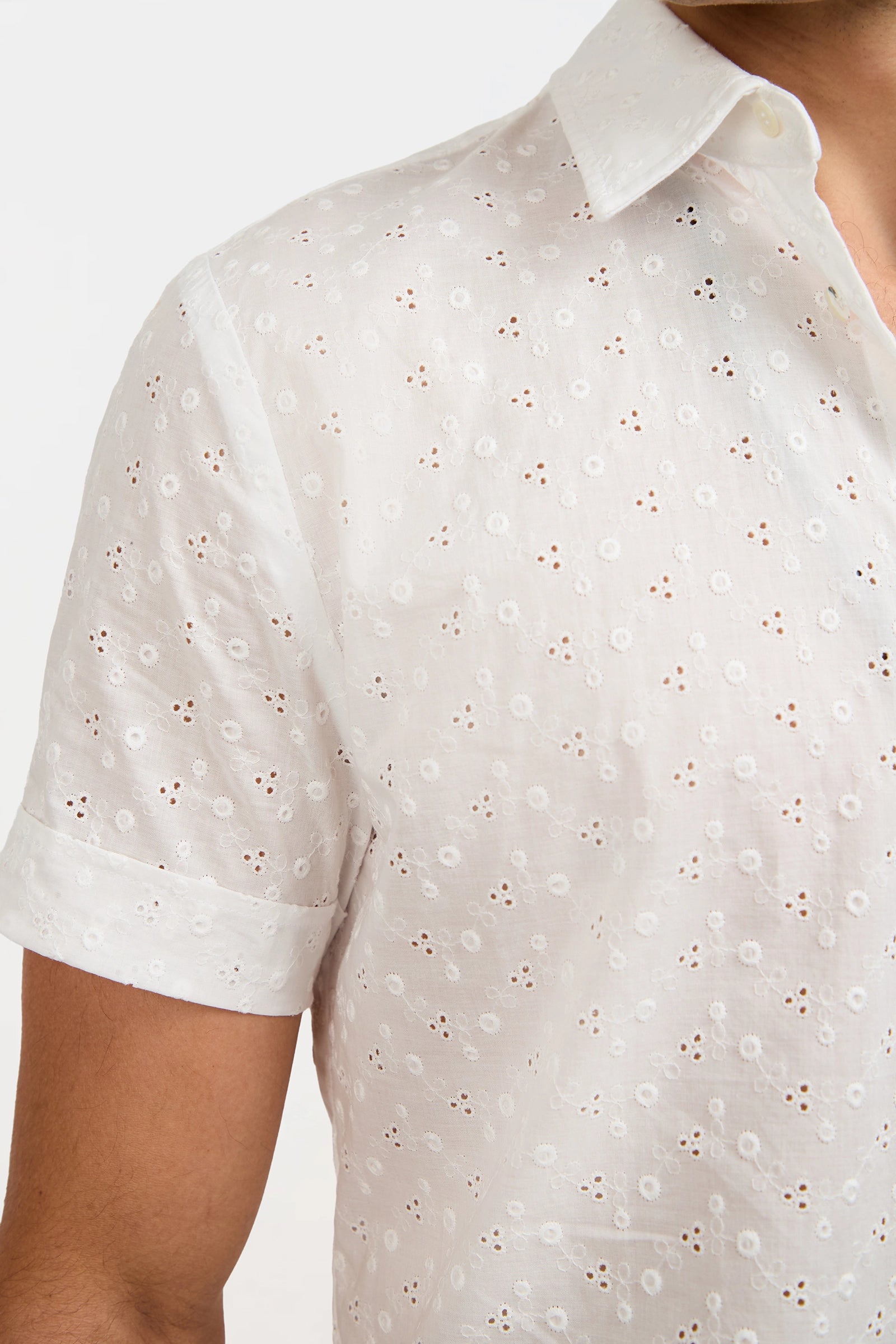 A close-up of a person wearing the Branson Short-Sleeve Shirt, a white semi-transparent eyelet top with floral embroidery and a collar, subtly revealing skin underneath.