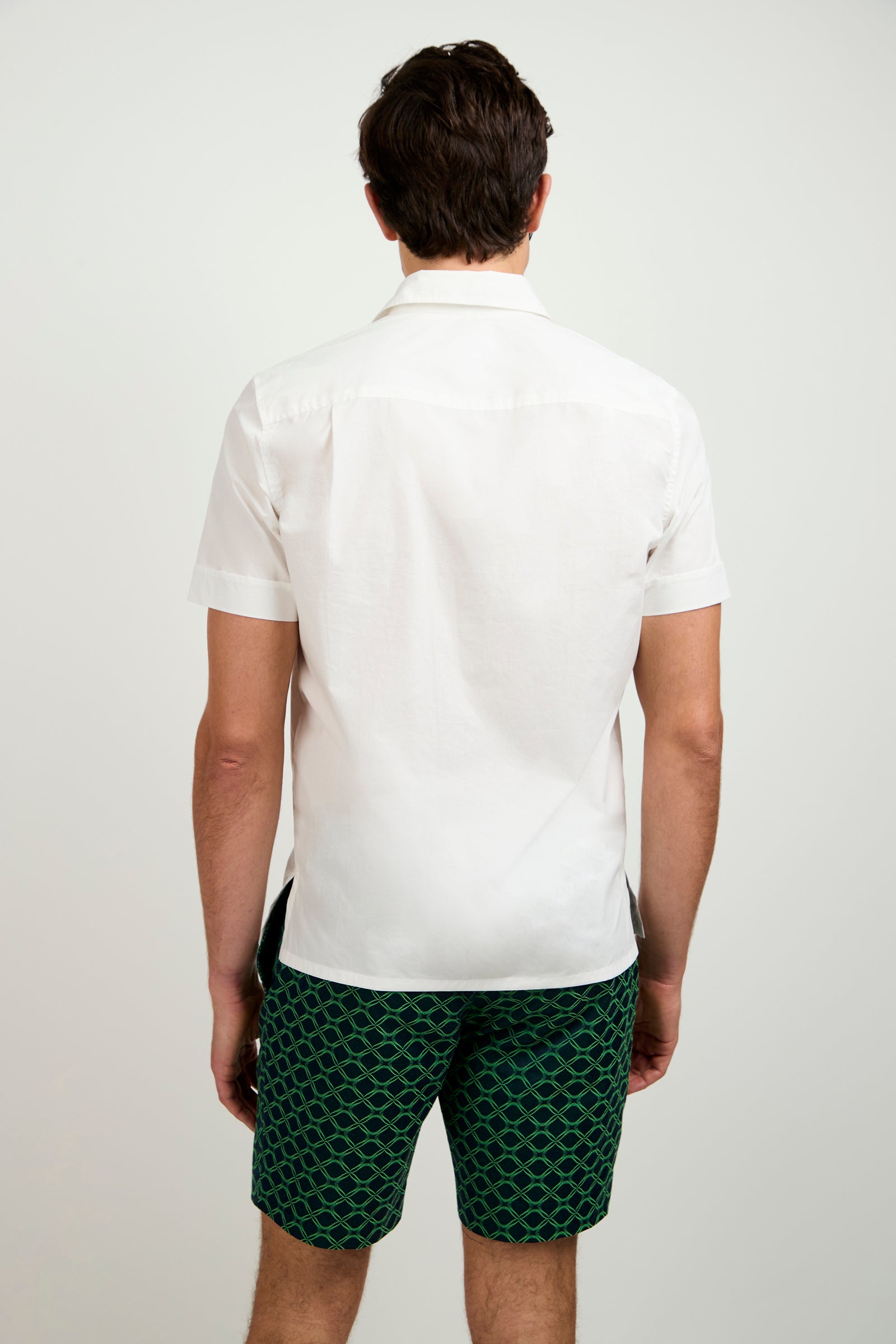 A man stands with his back to the camera, wearing the Will Short-Sleeve Shirt in white and green patterned shorts, set against a plain light background.