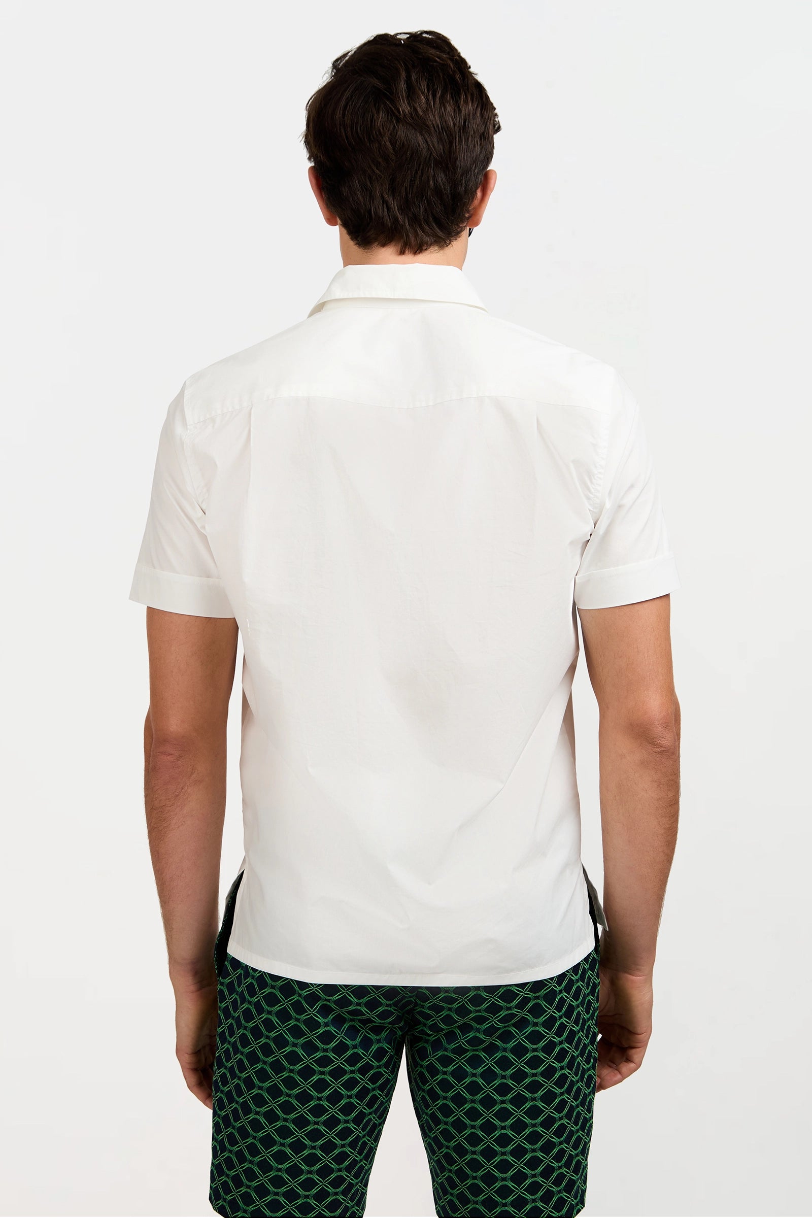 A man is seen from behind against a white background, wearing the Will Short-Sleeve Shirt in white and green shorts with a black geometric pattern.