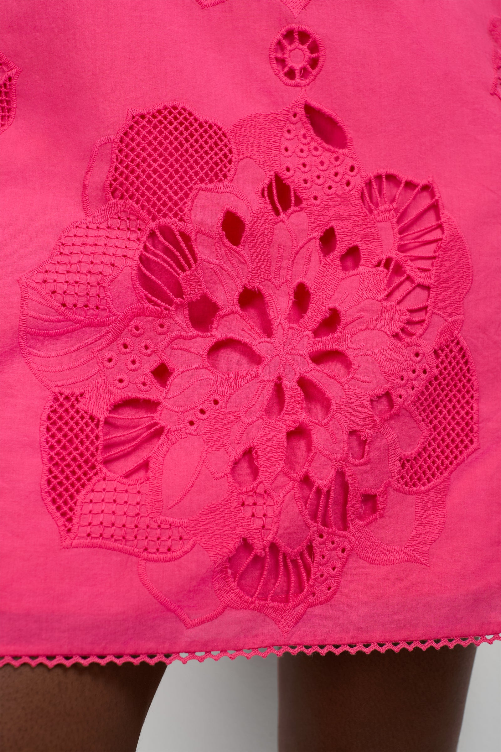 Close-up of the Francesca Shift Dress in vibrant pink, showcasing intricate floral cutout embroidery and scalloped hem, with dark skin visible beneath the detailed cutouts.
