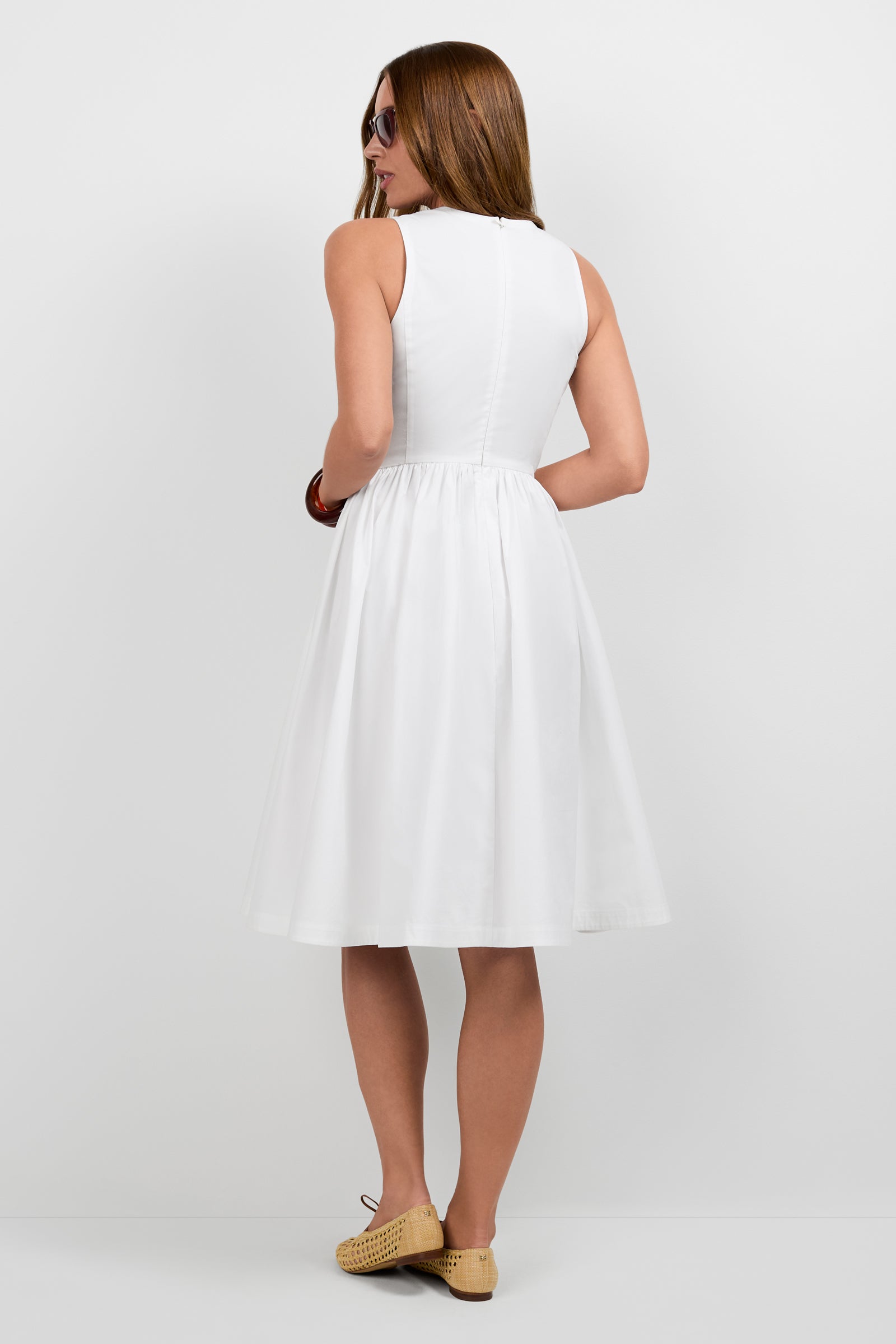 A woman with straight brown hair, wearing sunglasses and the Lombardy Midi Dress with beige flats, stands with her back to the camera against a plain white background.