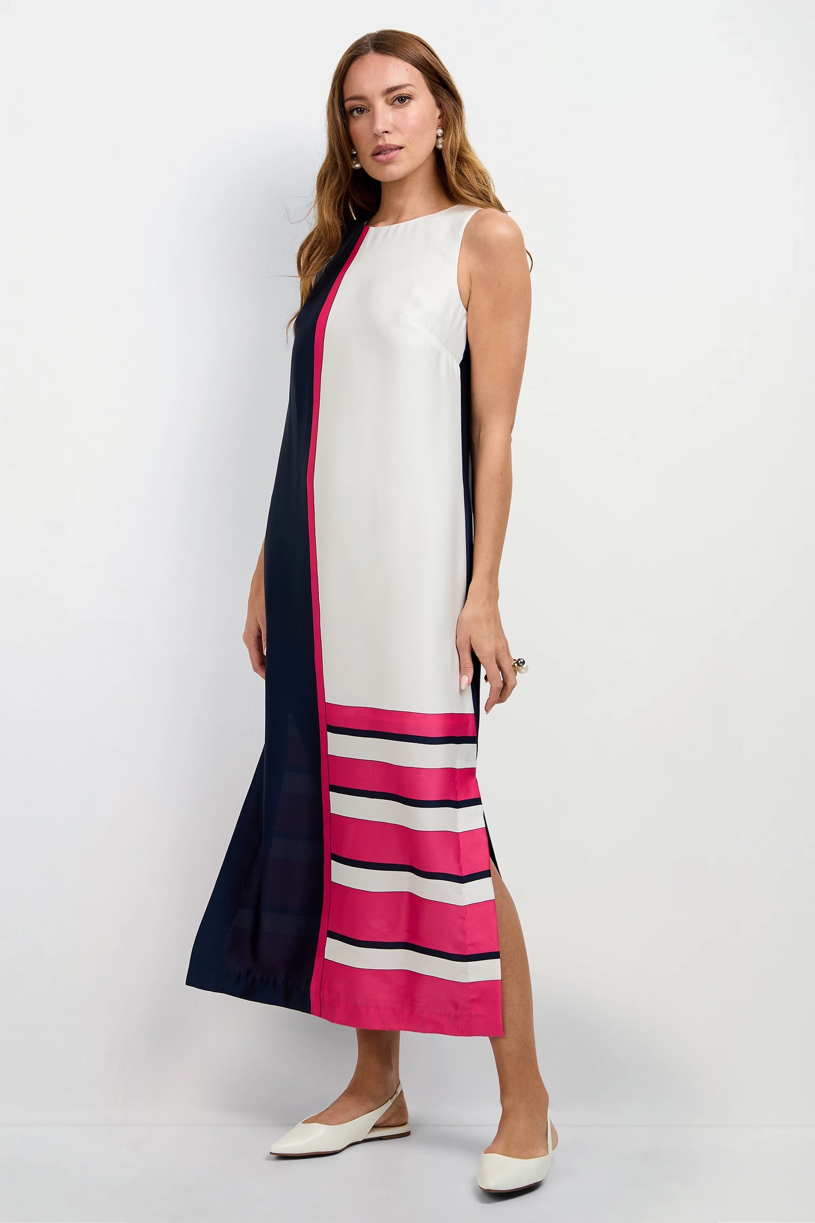 A woman models the Moderna Linee Midi Dress—sleeveless, ankle-length, navy blue and white color block with pink stripes at the hem—paired with white flats, standing against a plain white background.
