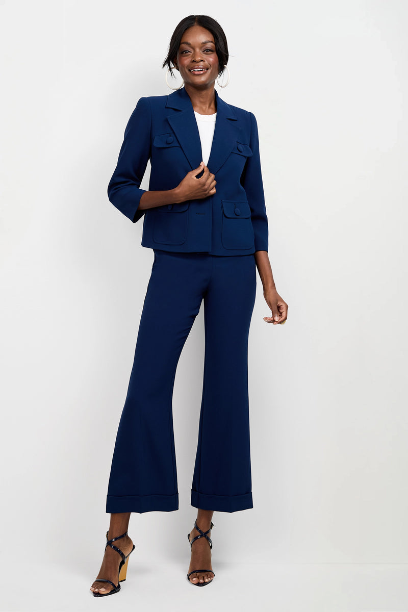 A woman smiles in the Bicocca Patch Pocket Jacket, styled with navy blue flared pants, a white top, and black high-heeled sandals against a plain white background.