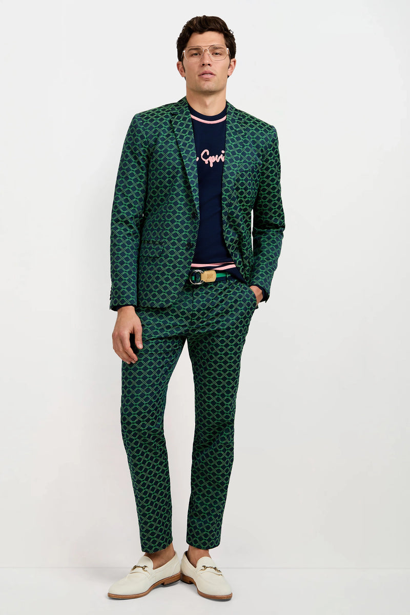 A man wearing a green patterned suit, the Palm Springs Crewneck Sweater, white loafers, glasses, and a tan belt stands against a plain white background.