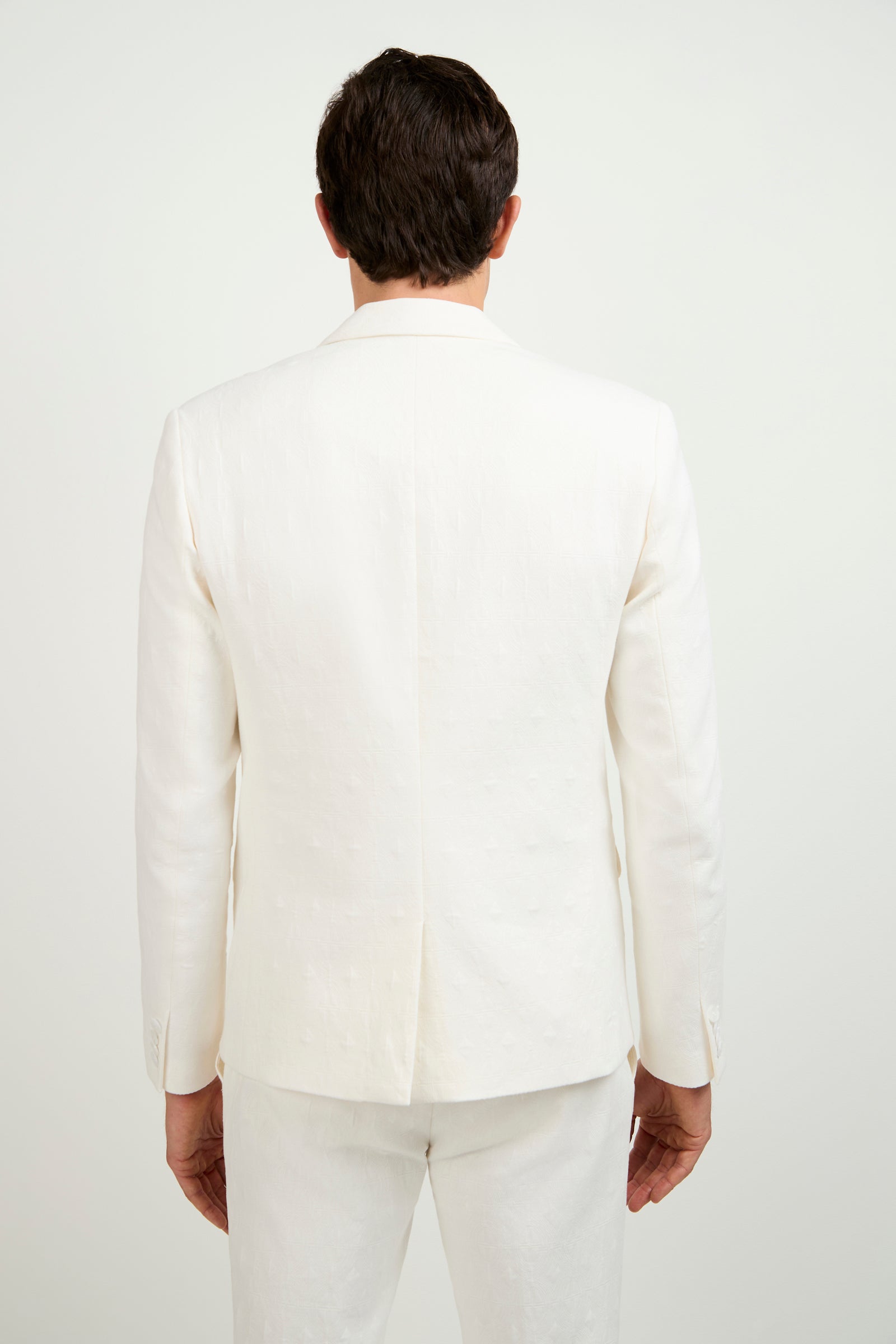 A man stands facing away from the camera, wearing the Thurston Blazer in Tegola Textured Jacquard and matching white pants against a plain white background.