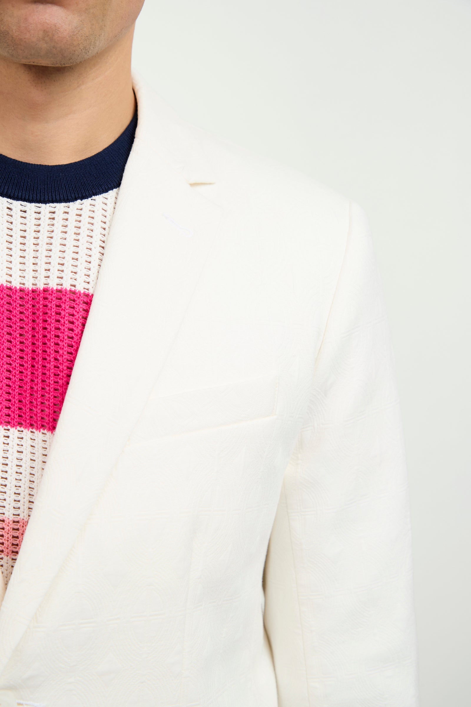 A man wears the Thurston Blazer in Tegola Textured Jacquard over a pink and navy striped knit sweater, set against a plain light background. Only the lower half of his face and upper torso are visible.