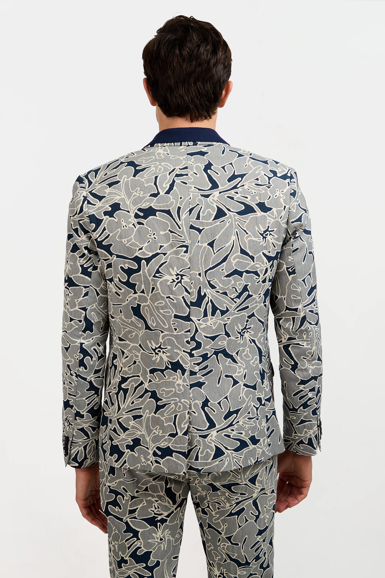 A man faces away, wearing the Thurston Blazer in an artsy blue and light gray floral jacquard, set against a plain white background.