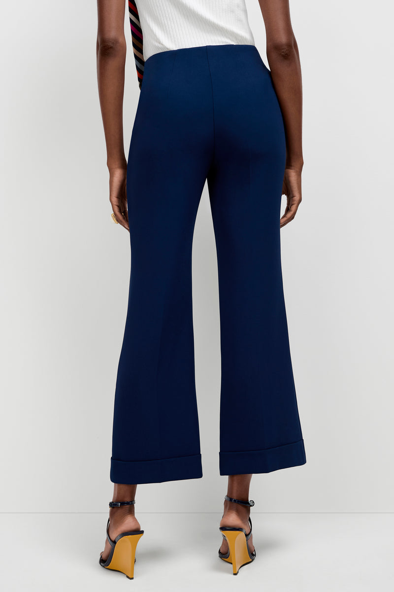A person is seen from the back wearing Loren Cropped Kick-Flare Pants in dark blue with black heeled sandals featuring yellow soles, standing against a plain white background.