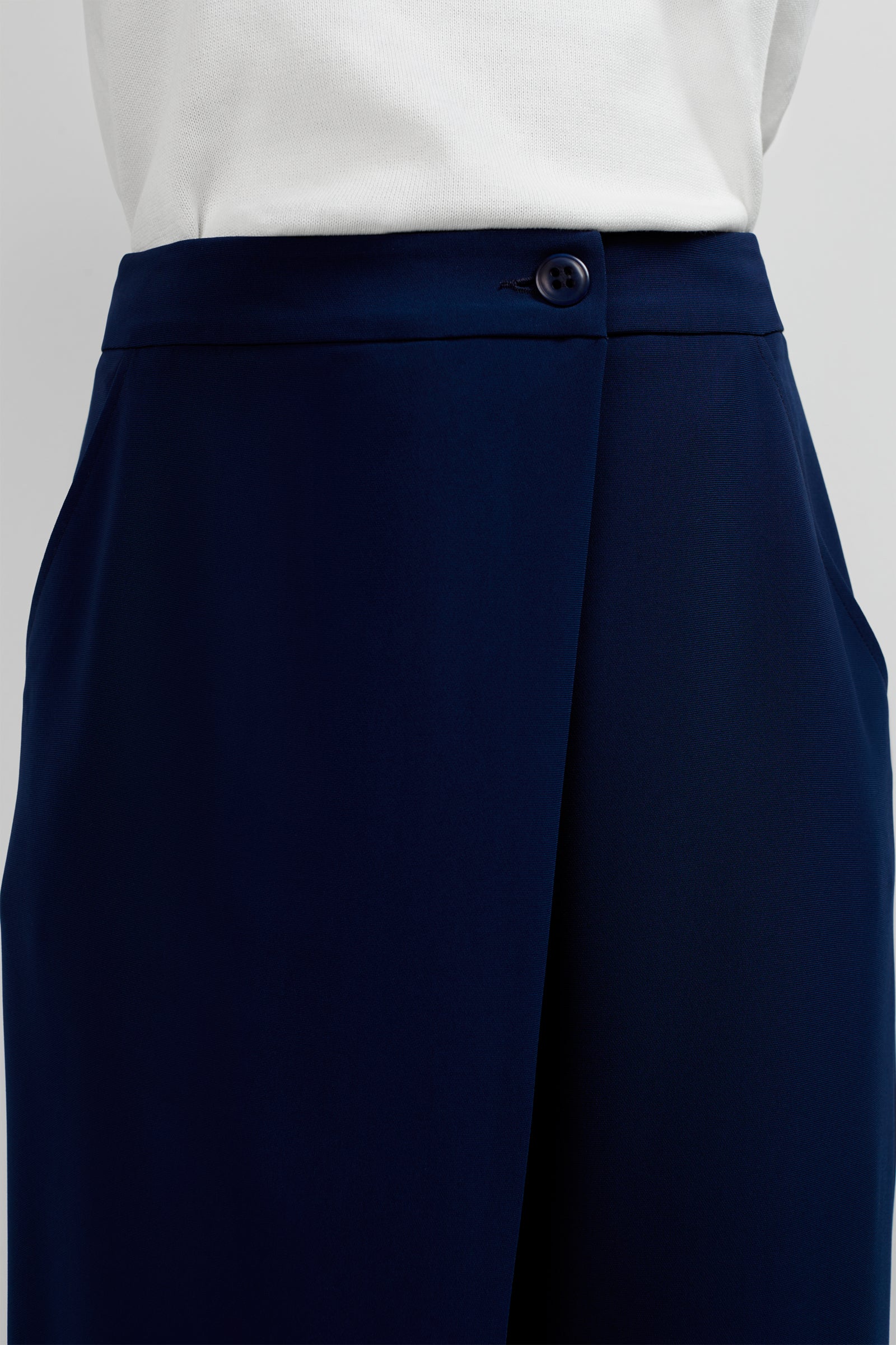 Close-up of a person wearing the Conchetta Wide-Leg Pants in dark navy blue, styled high-waisted with a button closure and side pockets, paired with a white top.