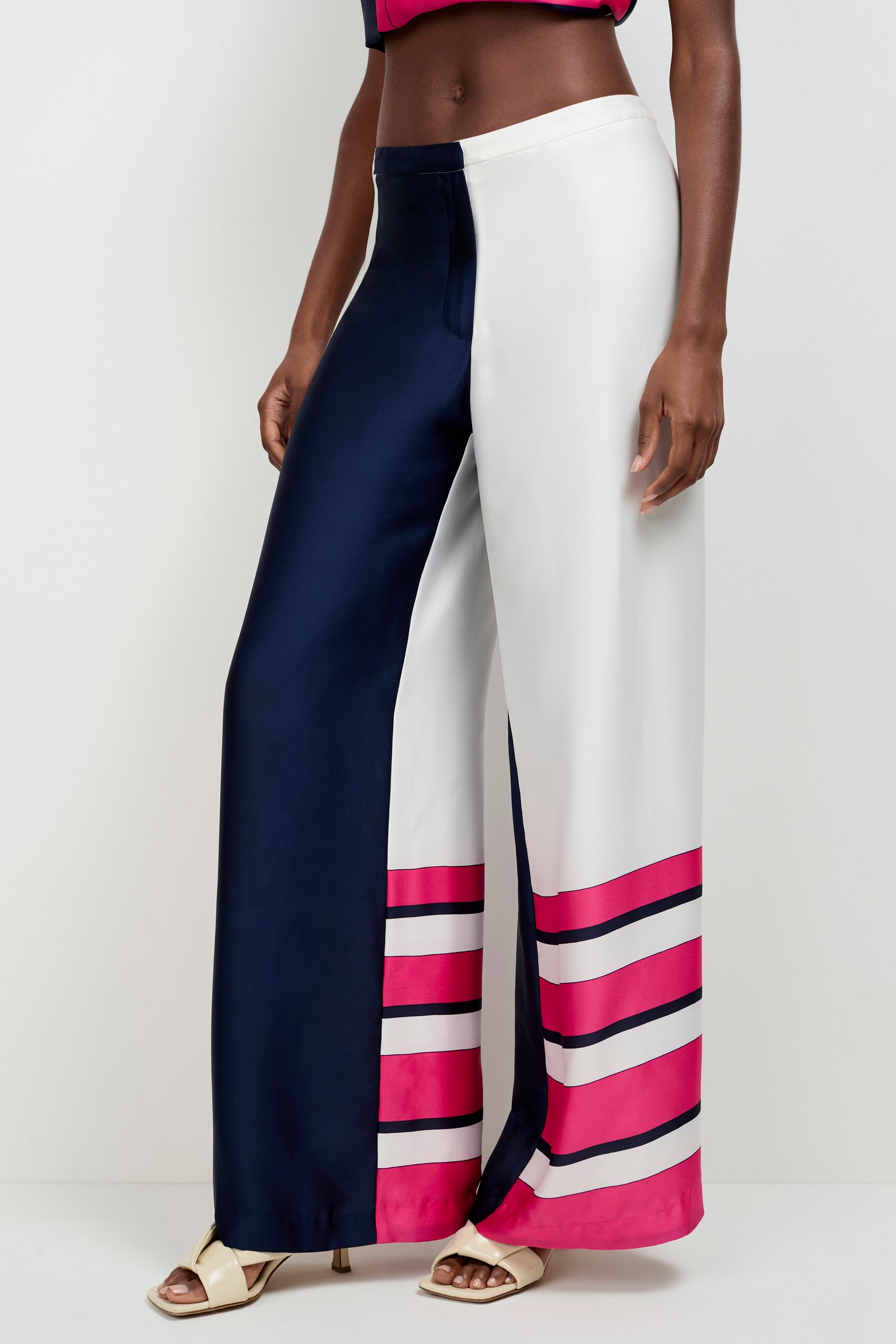 A person wearing the Lanay Linee Wide-Leg Panta, with one navy blue side and one white side, pink and navy horizontal stripes near the hem, paired with open-toe sandals.