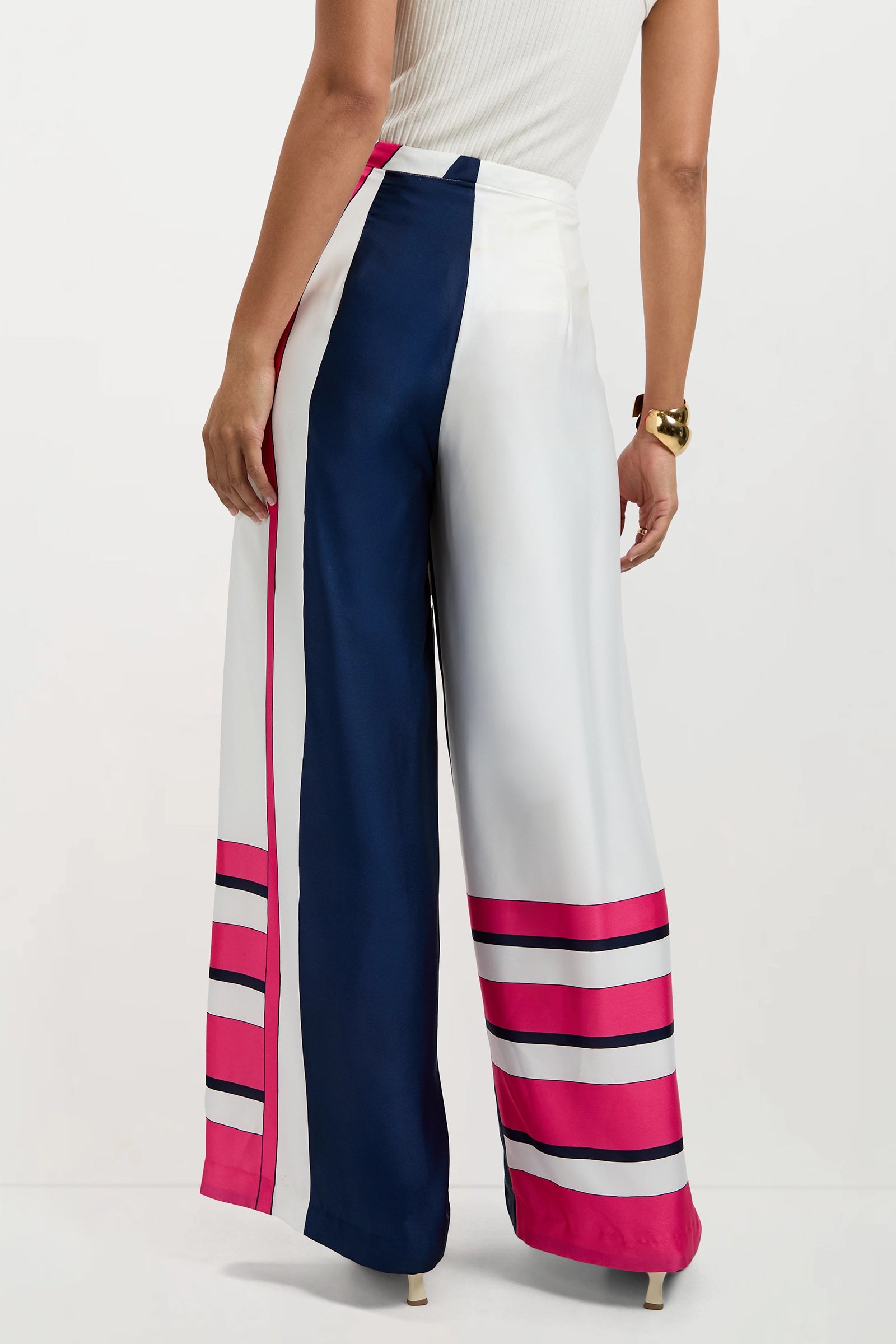 A woman stands with her back to the camera, wearing the Lanay Linee Wide-Leg Pants featuring high-waisted, wide-leg color-blocked panels in navy blue, white, and pink with horizontal pink stripes near the hem and a sleeveless white top.
