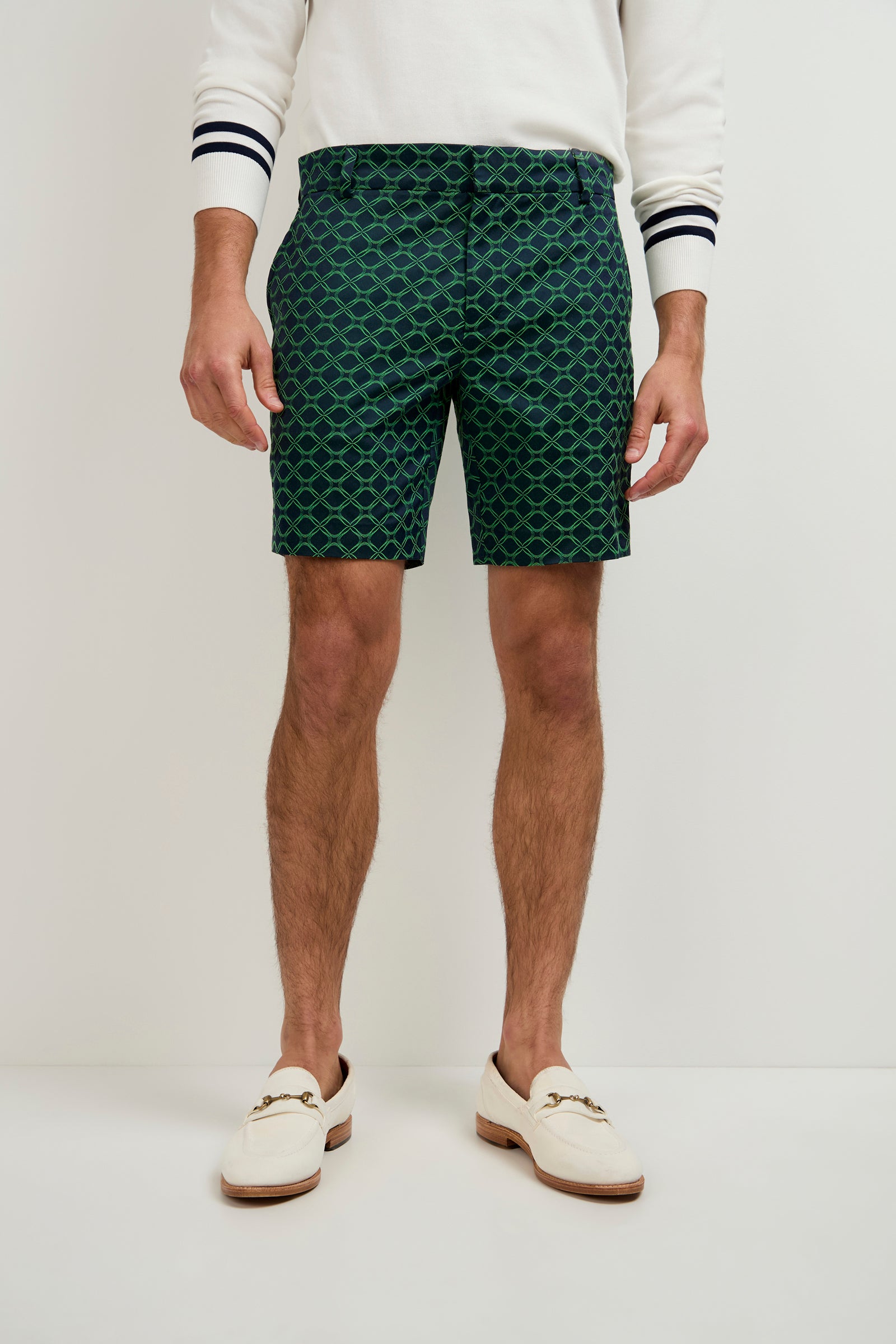 A person stands against a plain white background wearing a white long-sleeve sweater with dark striped cuffs, Lawrence Short - Clover Geo Jacquard in INK MULTI, and white loafers.