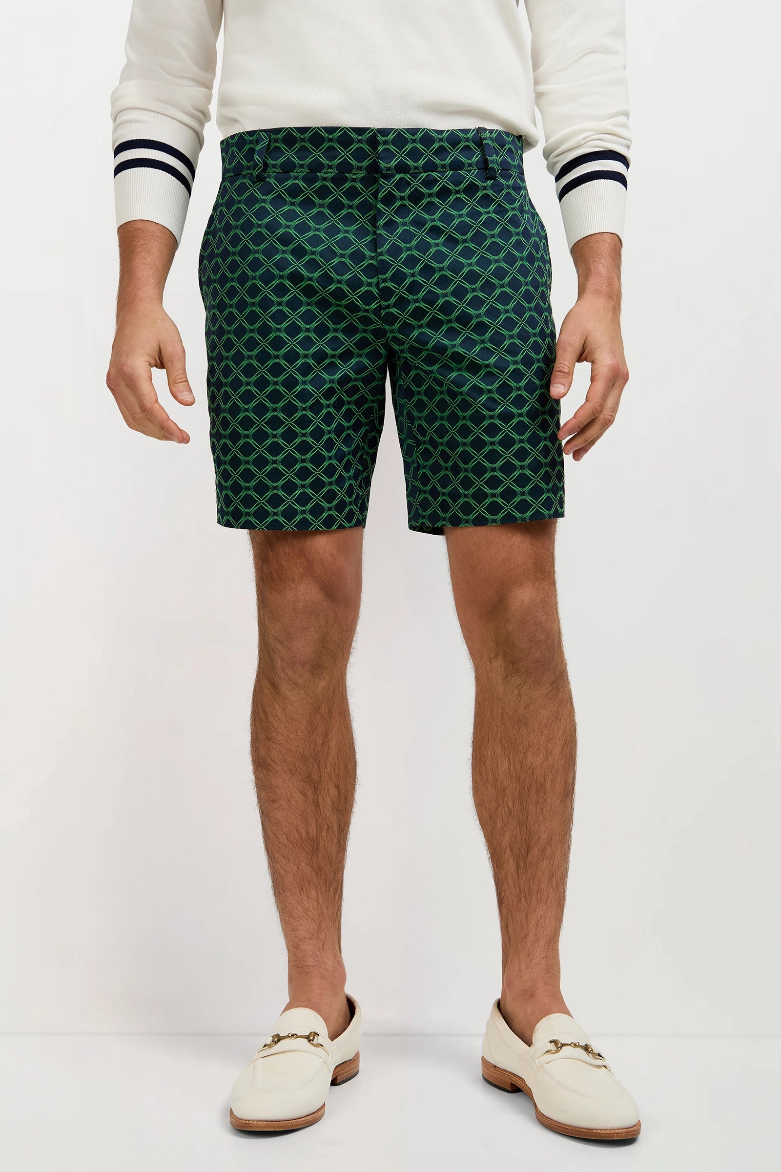 A man models the Lawrence Short - Clover Geo Jacquard paired with a white sweater and white loafers against a plain background. His head is not visible in the image.