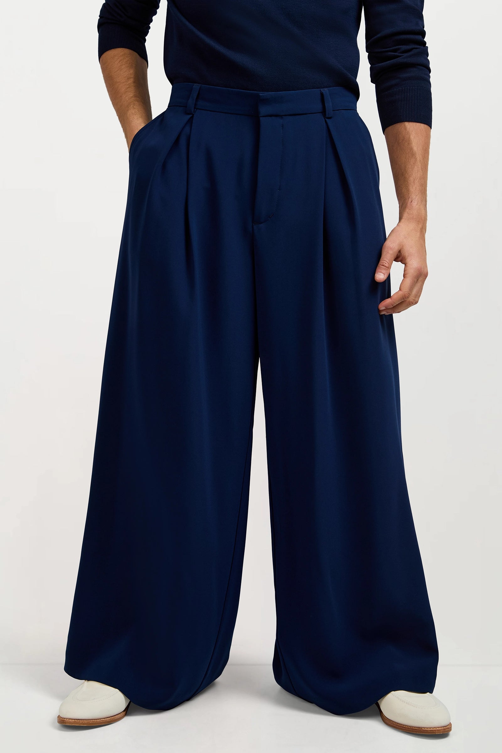 Only the lower half of a person is visible as they stand against a plain background, wearing navy Clyde Wide-Leg Trousers and white shoes.