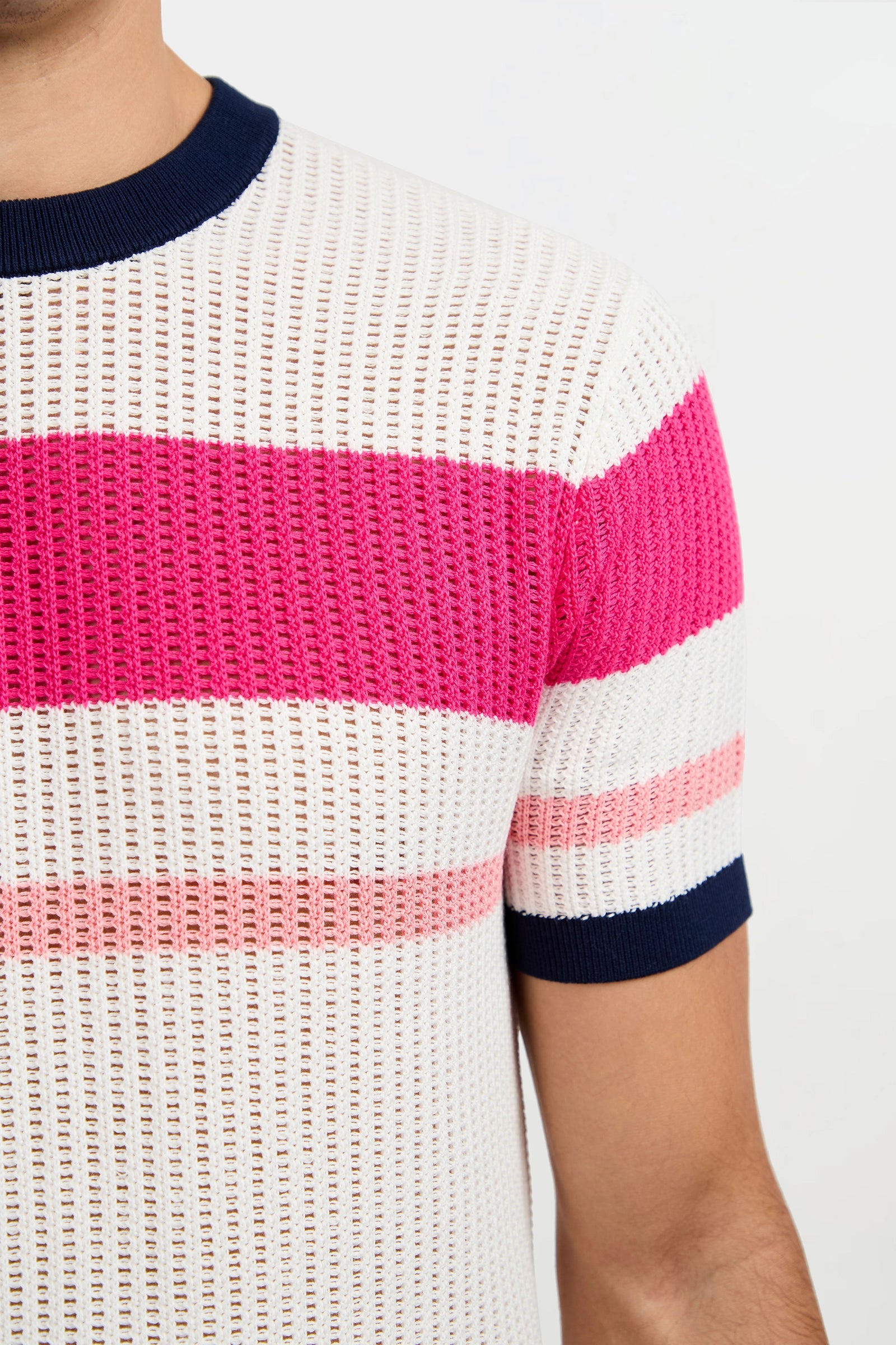 A person wearing the Aldo Short-Sleeve Crewneck, featuring wide pink and thin light pink horizontal stripes, a navy blue collar and cuffs, and a white mesh-like texture. The photo shows their upper torso against a plain background.