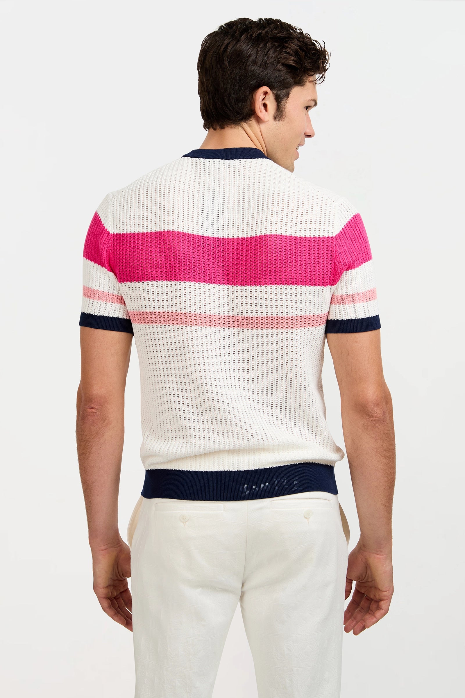 A man faces away, wearing the Aldo Short-Sleeve Crewneck—white with horizontal pink stripes and navy trim—paired with white pants against a plain white background.