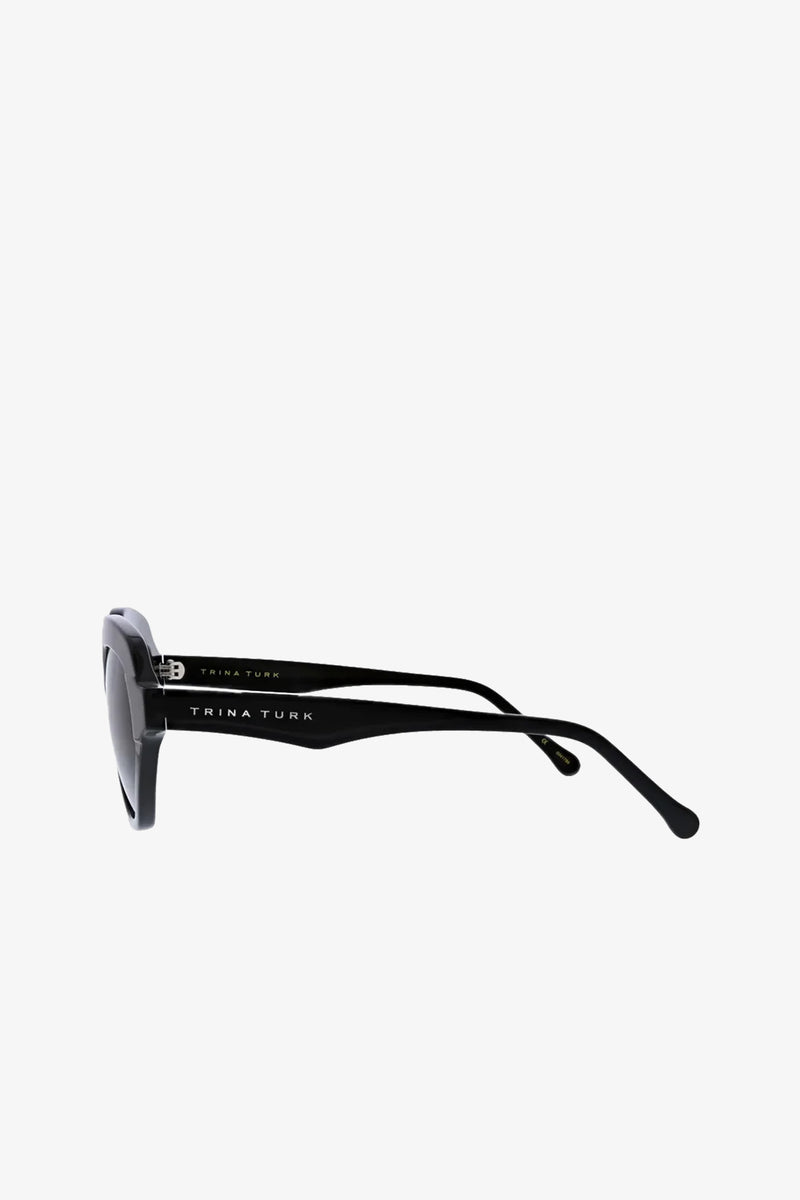Side view of black Ipanema Sunglasses with TRINA TURK written in white on the temple, set against a plain white background.