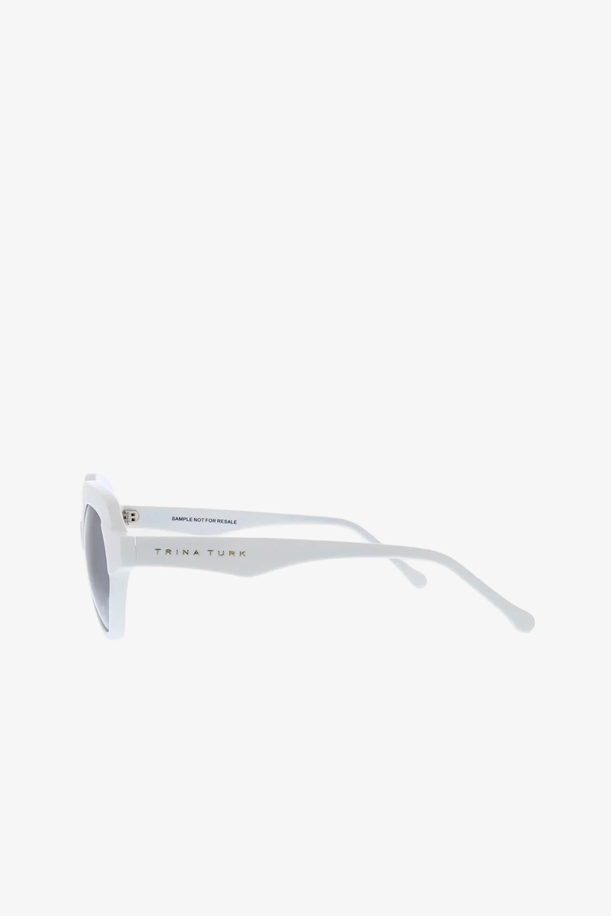 Side view of white-framed Ipanema Sunglasses with dark lenses. The brand name Trina Turk is printed on the arm in black letters, and the sunglasses are set against a plain white background.