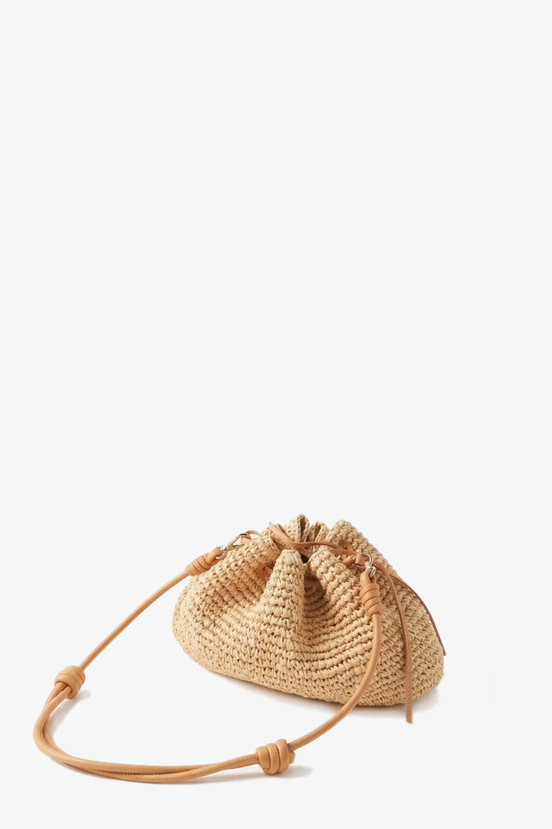 The Kayu Canary Drawstring Bag is a small, natural-colored woven straw pouch with a drawstring closure and a long tan leather strap, shown against a plain white background.