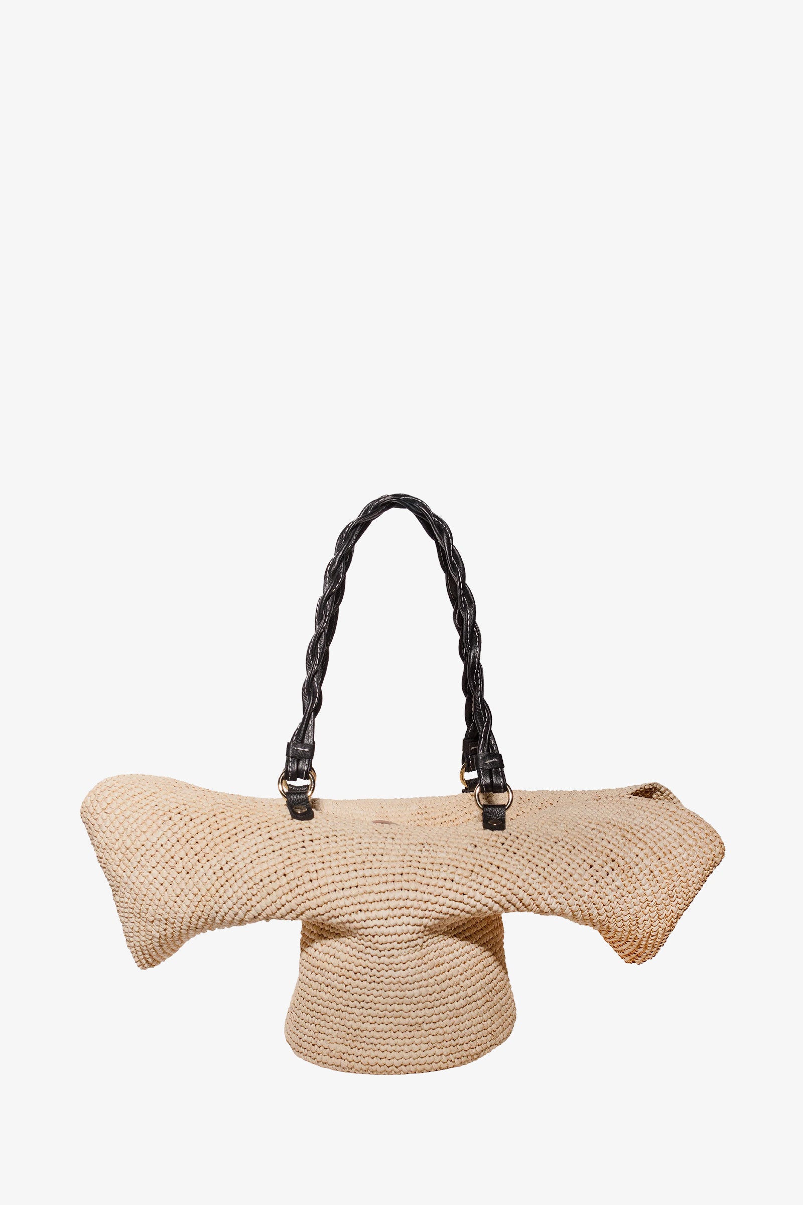 The Hat Tote is a natural-colored woven straw handbag featuring an abstract, sculptural shape and two twisted black handles, shown against a plain white background.