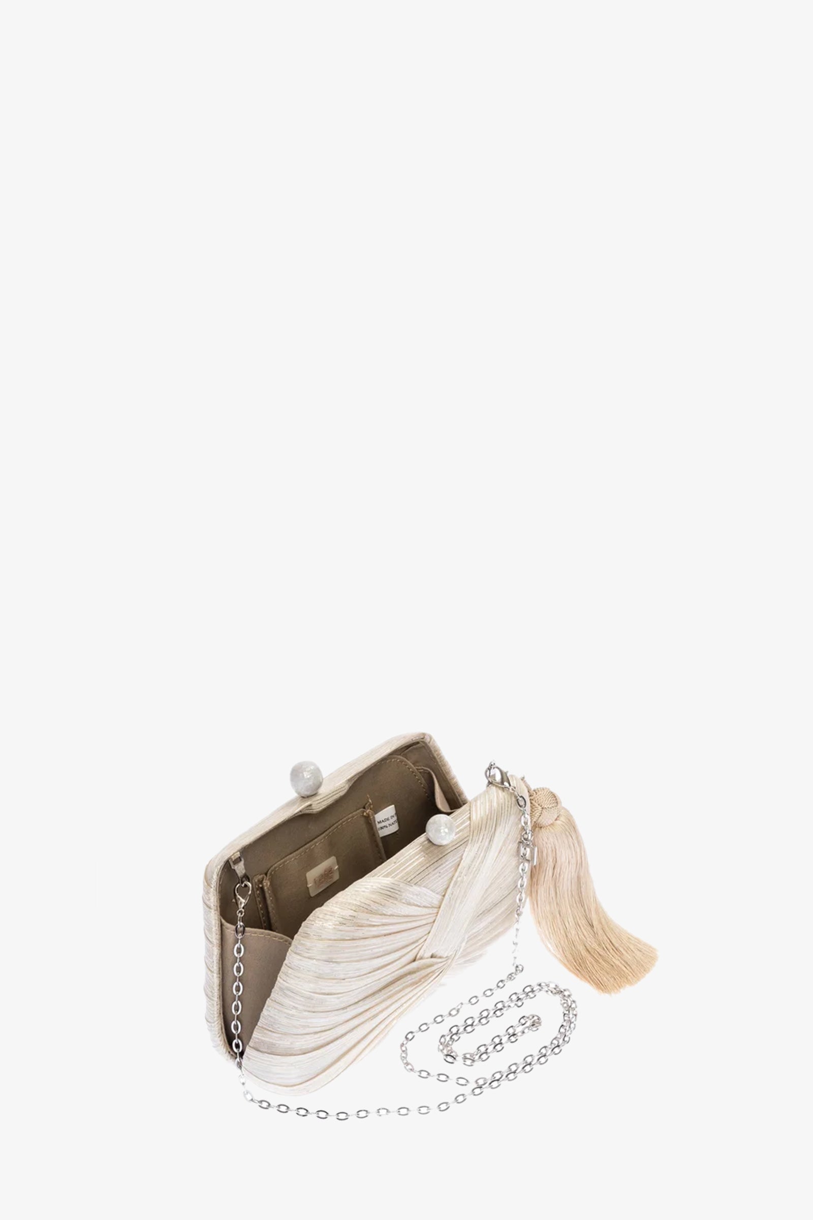 The Rosie Draped Clutch is a small, elegant beige purse with a wavy texture, metal clasp, long silver chain strap, and large beige tassel. Opened, it reveals a tan interior with pockets.