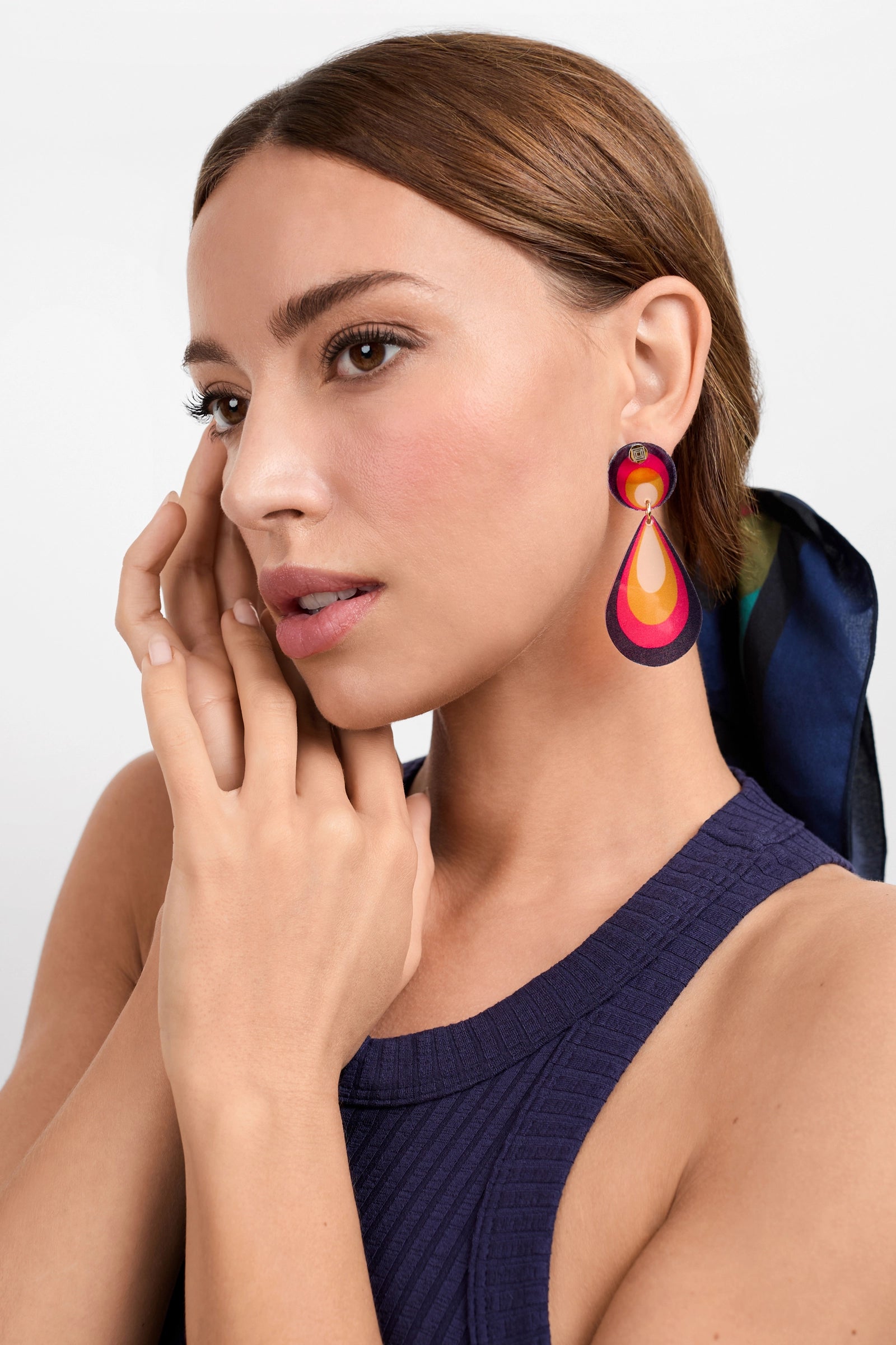 A woman with light skin and brown hair poses with her hand near her face, wearing a sleeveless navy top and Cascade Drop Earrings. She has a dark scarf in her hair, against a plain white background.