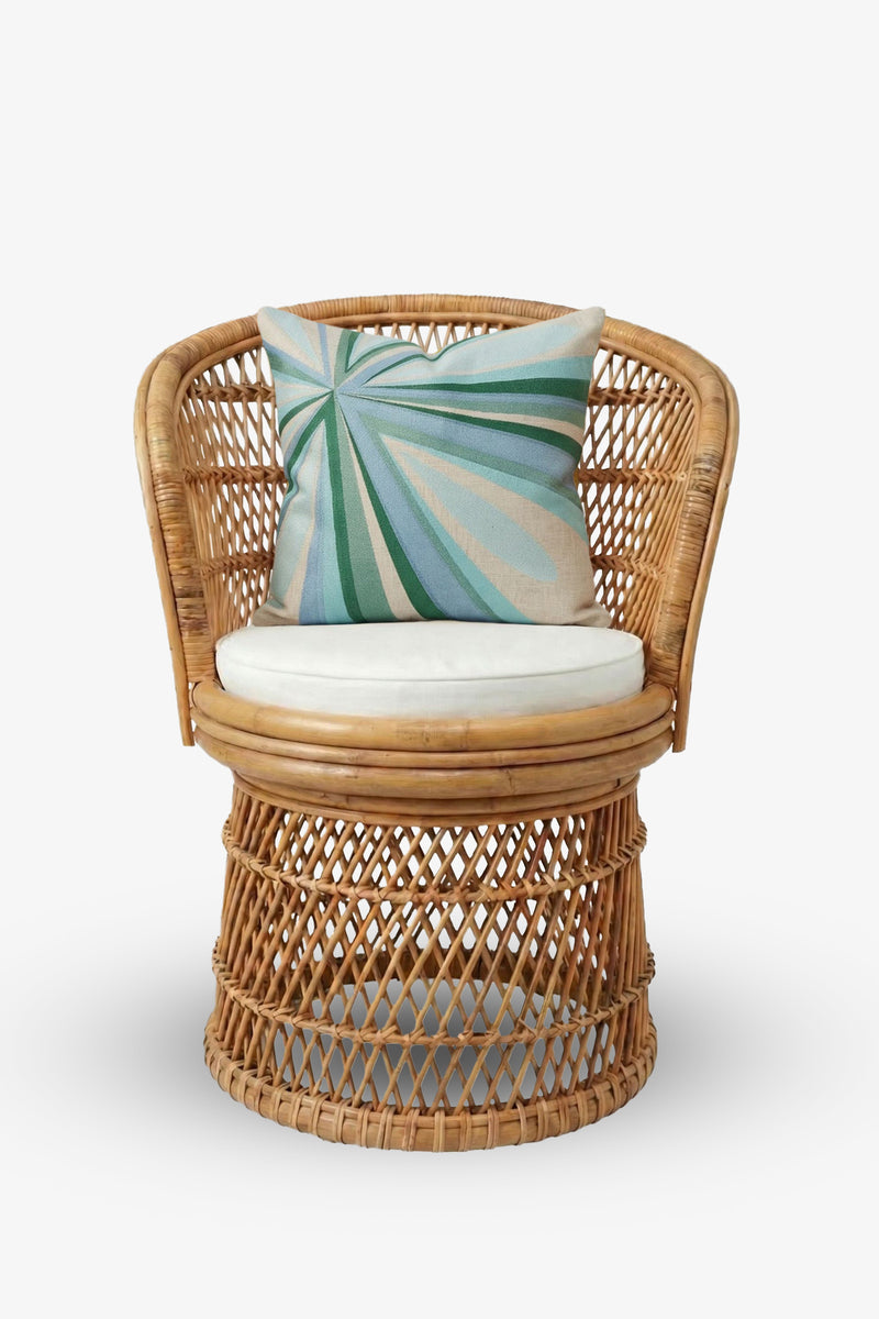 A round rattan chair with a white seat cushion and the Shante Embroidered Square Pillow, featuring green and blue leaf patterns, set against a plain white background.