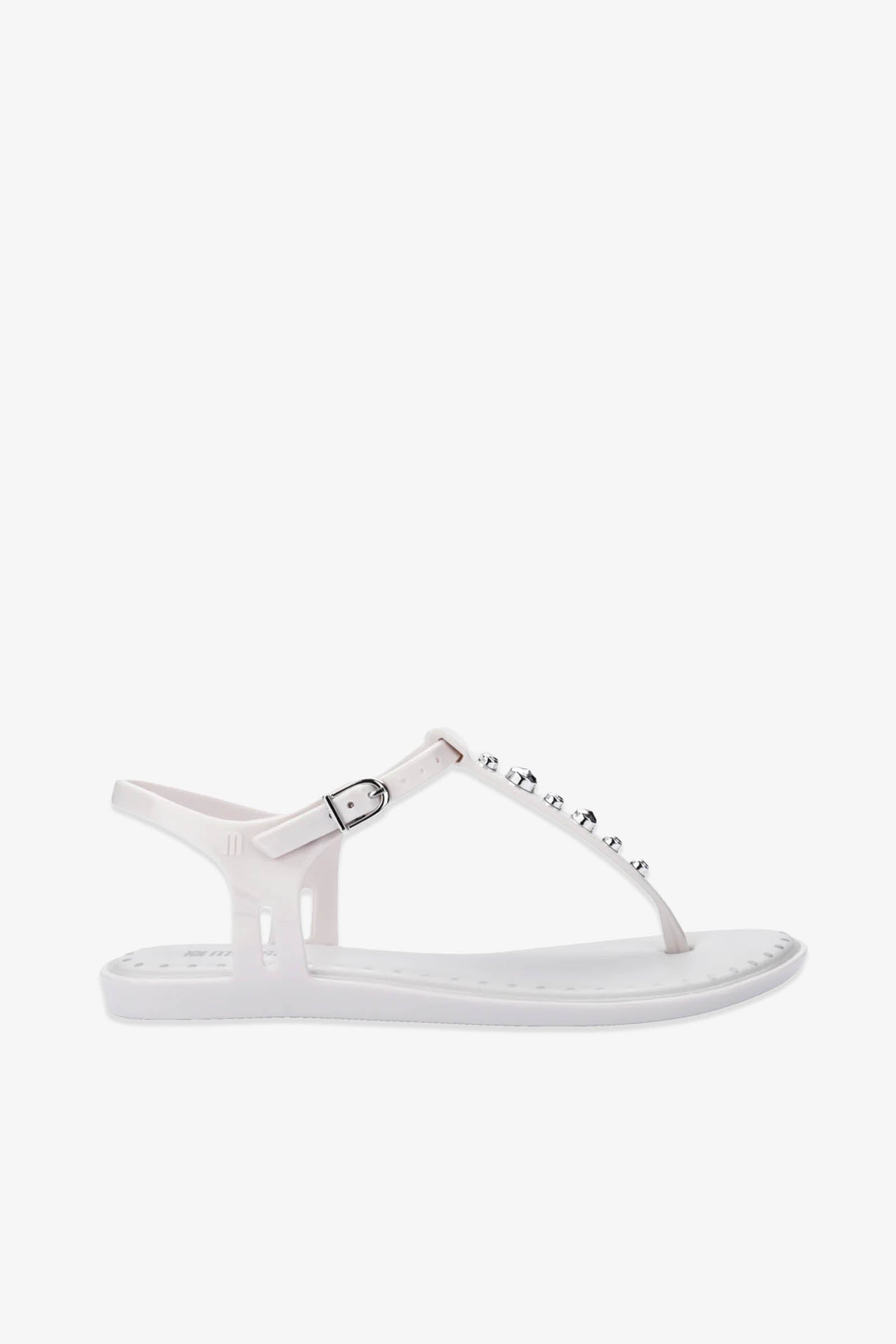 Solar Boho Thong Sandals in white featuring a flat sole, ankle strap with silver buckle, and silver studs embellishing the T-strap. Showcasing a simple, minimalist design on a plain white background.