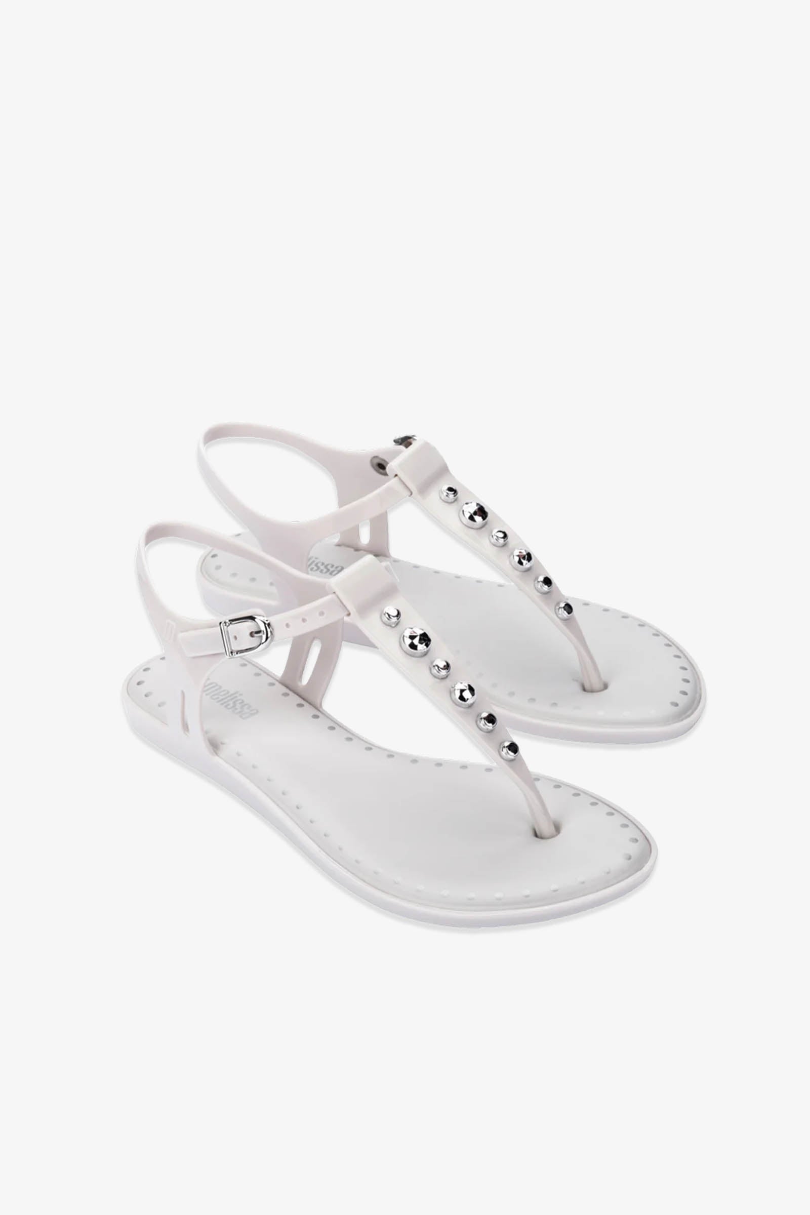 A pair of Solar Boho Thong Sandals in white, adorned with silver studs on the straps, featuring ankle straps and a flat sole, displayed on a plain white background.
