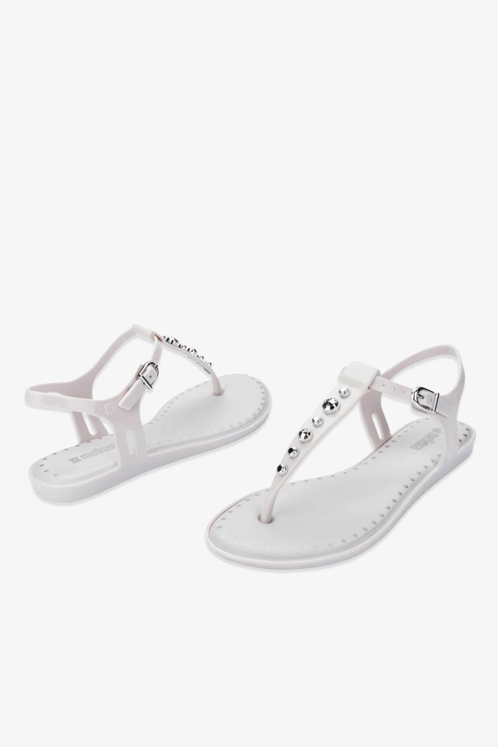 A pair of Solar Boho Thong Sandals in white, featuring ankle straps and silver studs adorning the top, displayed from both side and front angles against a plain white background.